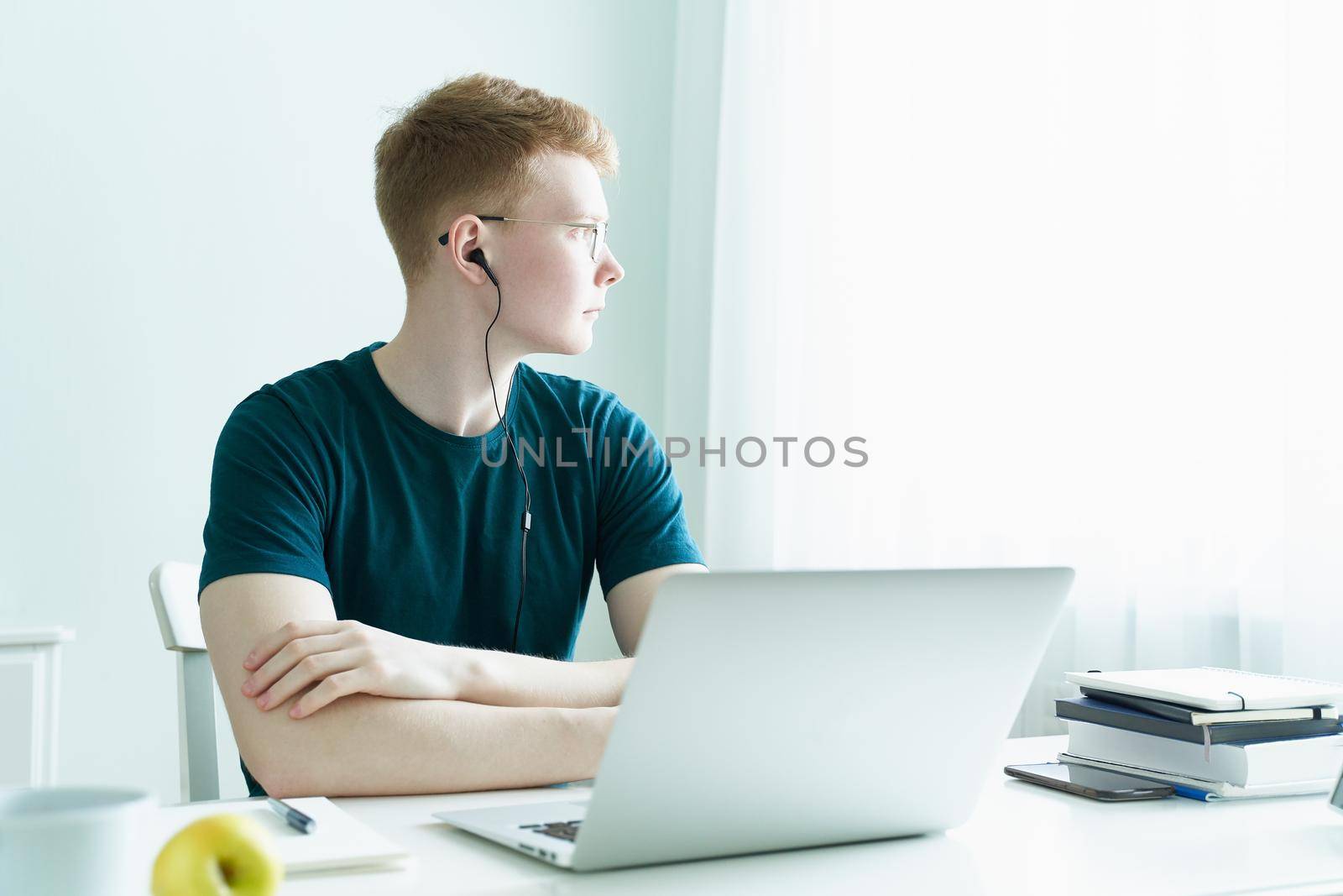 Young man listens to music and looks out window, sitting at computer. Distance learning or working. Quarantine, self-isolation, social phobia. Freelancer, Concept Of Digital Nomad