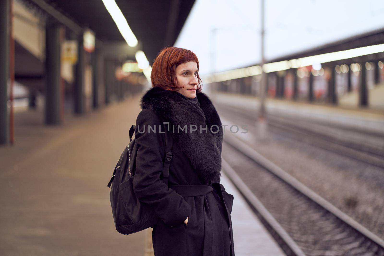 Railway station. Beautiful girl is standing on platform and waiting for train. Woman travels light in evening. Middle-aged lady in warm clothes, coat, in winter. Banner