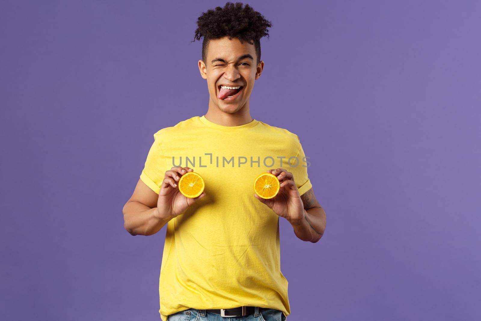 Holidays, vitamins and vacation concept. Portrait of sassy and cheeky funny young playful guy, fool around with fruit, holding pieces of oranges like women breast, show tongue smiling.