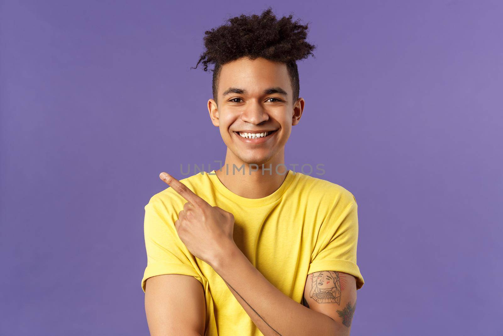 Close-up portrait of enthusiastic, happy young hipster male with dreads, beaming smile and pointing finger upper left corner, present cool product, introduce something really good, purple background.