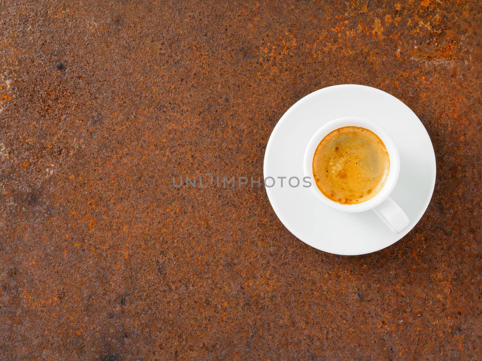 black frothy coffee with foam in white cup with plate on rusty metal table, top view, empty space for text by NataBene