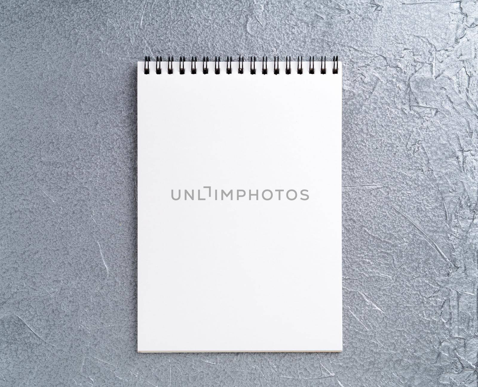 blank sheet of notebook with a spiral on a neutral gray textured silver metallic background