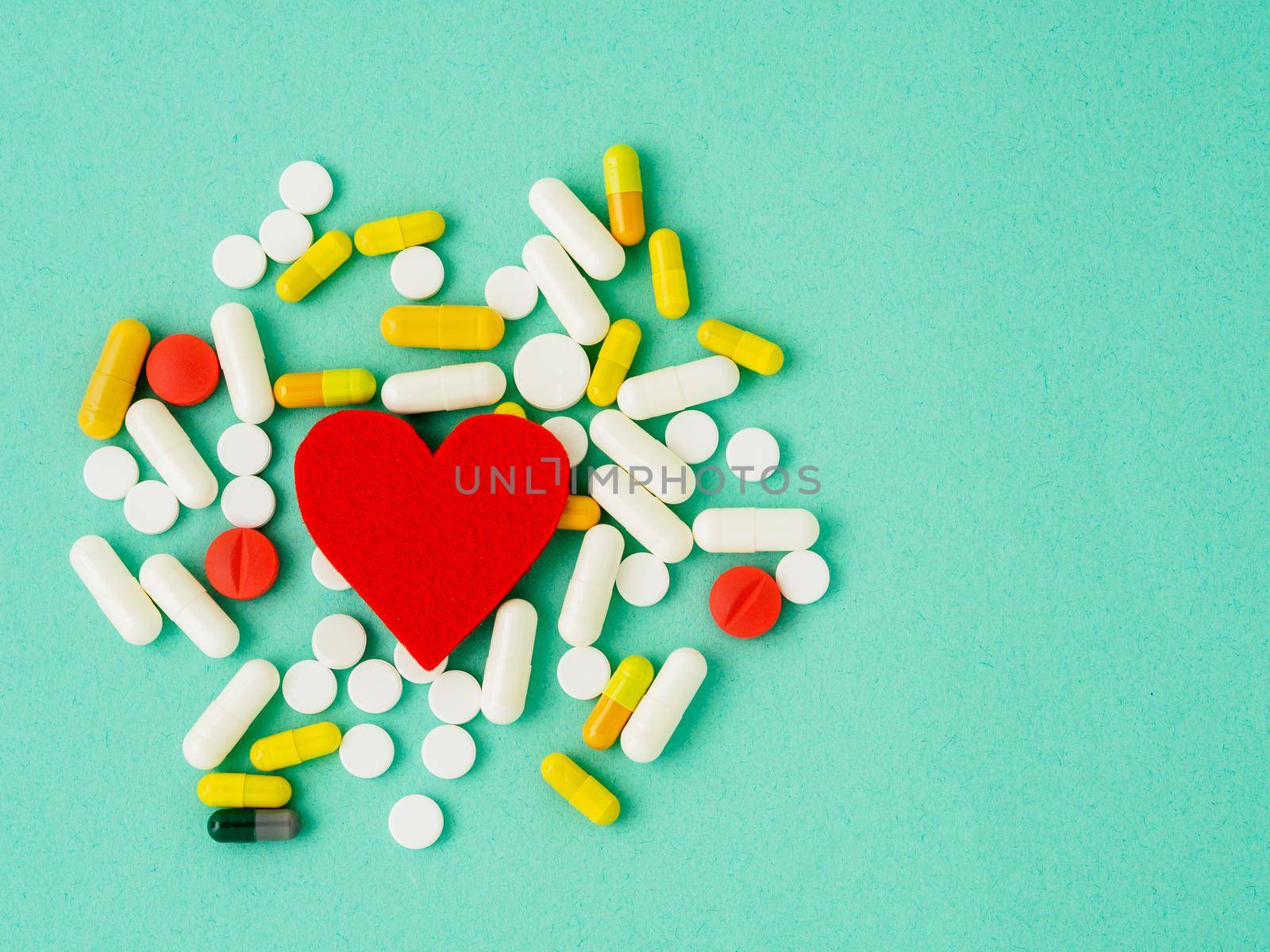 handful of pills and a red heart on a bright turquoise blue colour table, top view, copy space. Medicine help for heart health. by NataBene