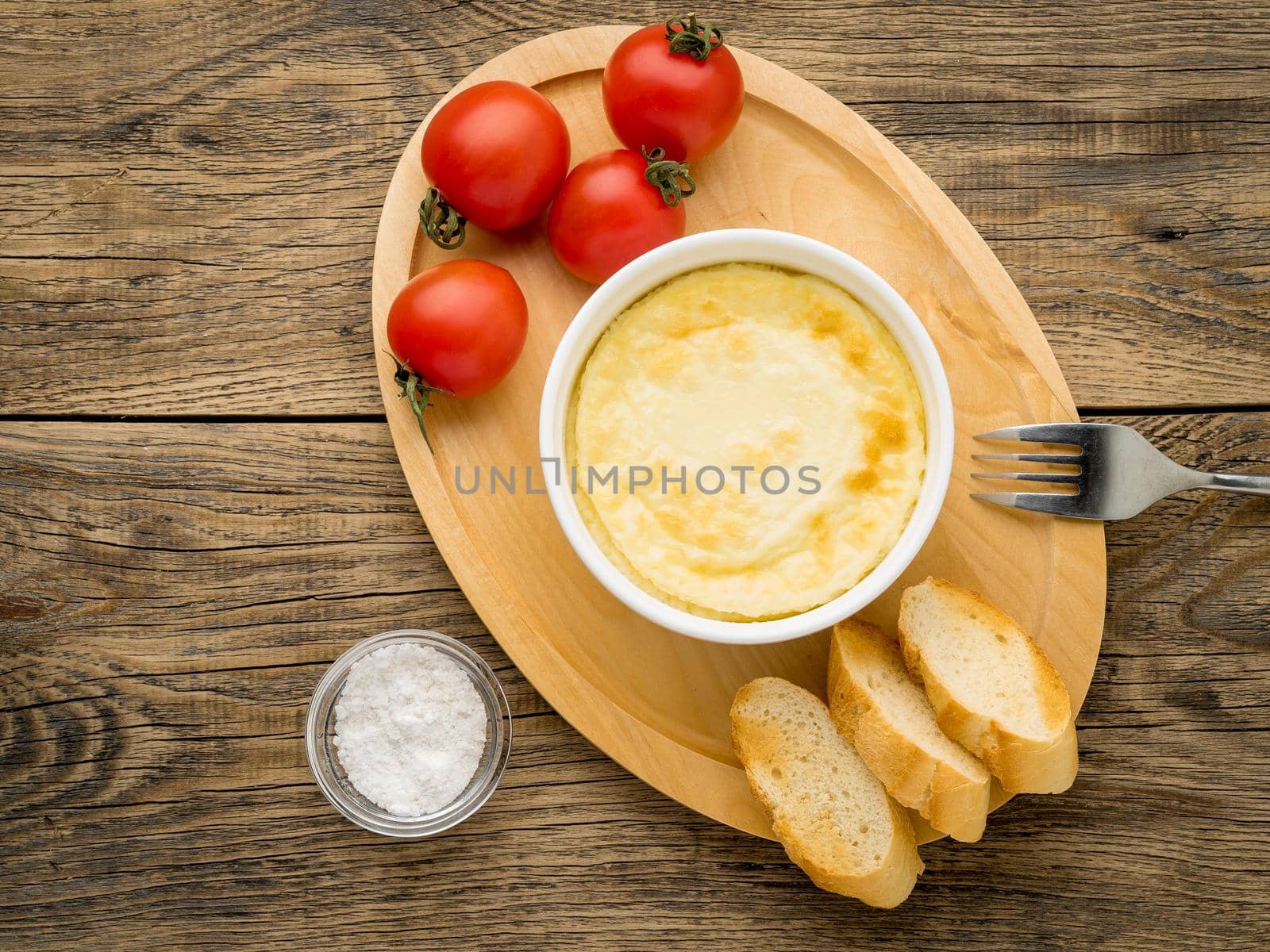 wood plate with oven-baked omelet of eggs and milk, with tomatoes and toast on brown rustic wooden table, top view