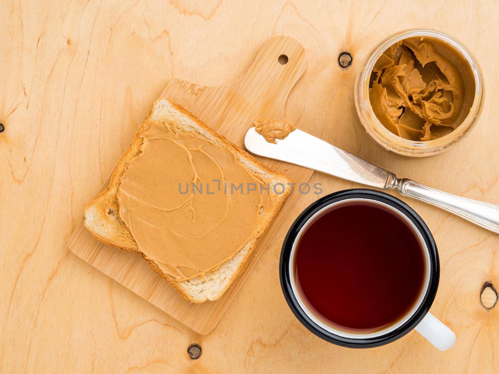 toast with peanut butter, knife for spreading on a sandwich, a mug of tea on a beige wood background by NataBene