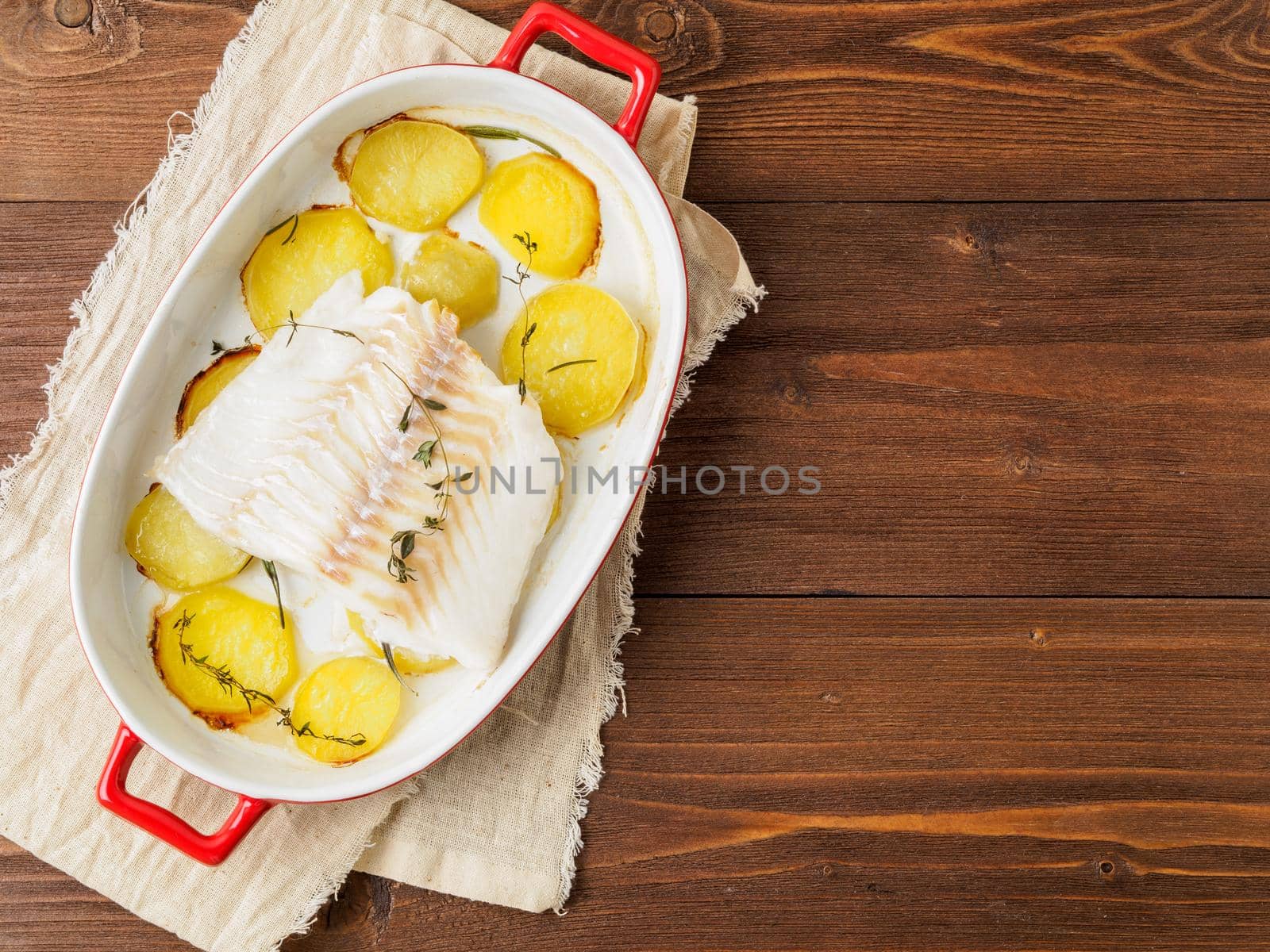 Fish cod baked in the oven with potatoes and spice and thyme - healthy diet healthy food. Dark wooden brown background, top view.
