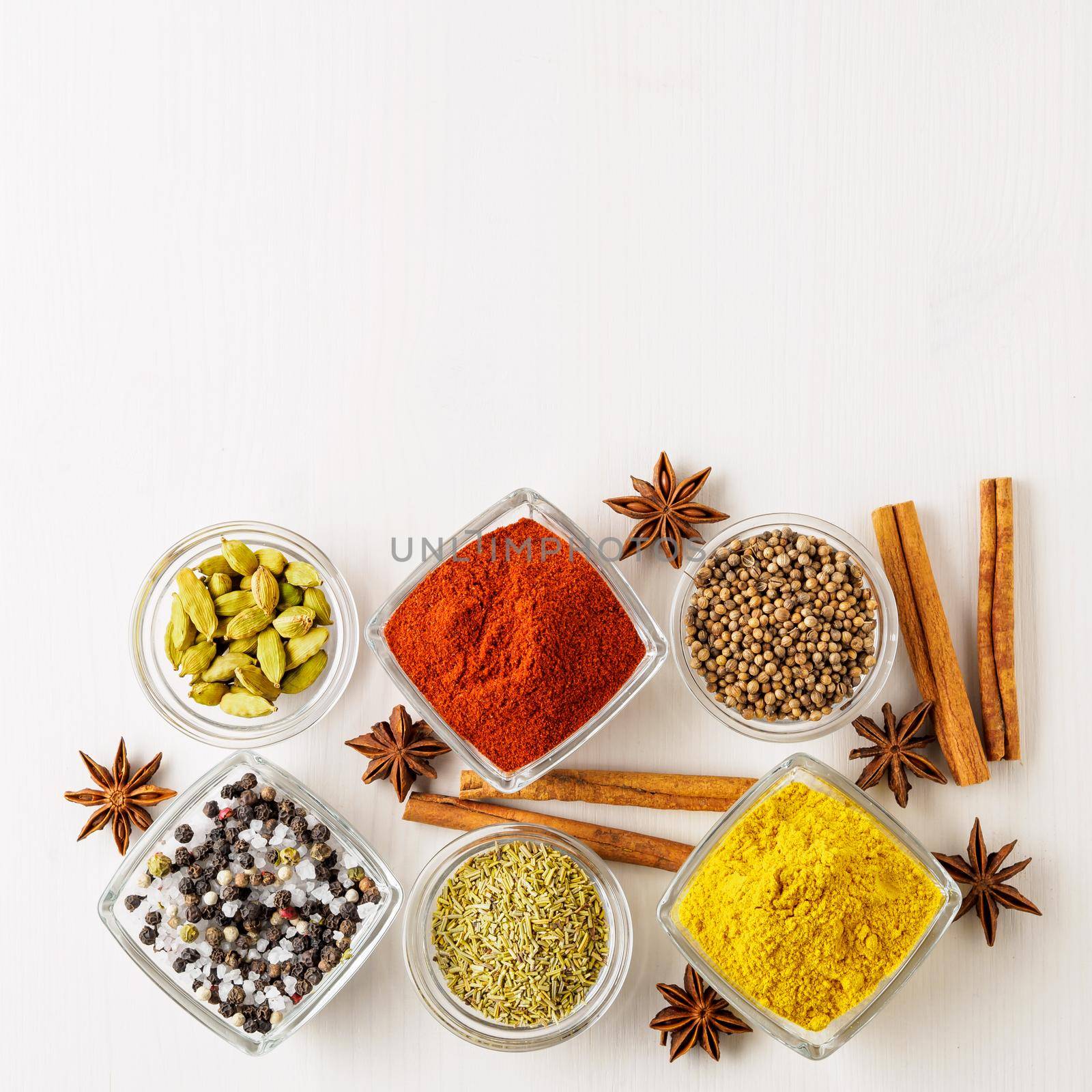 spice set-coriander, red pepper, turmeric, cinnamon, star anise, rosemary various seasonings in glass cups, on white wooden table, top view, blank space for text. by NataBene