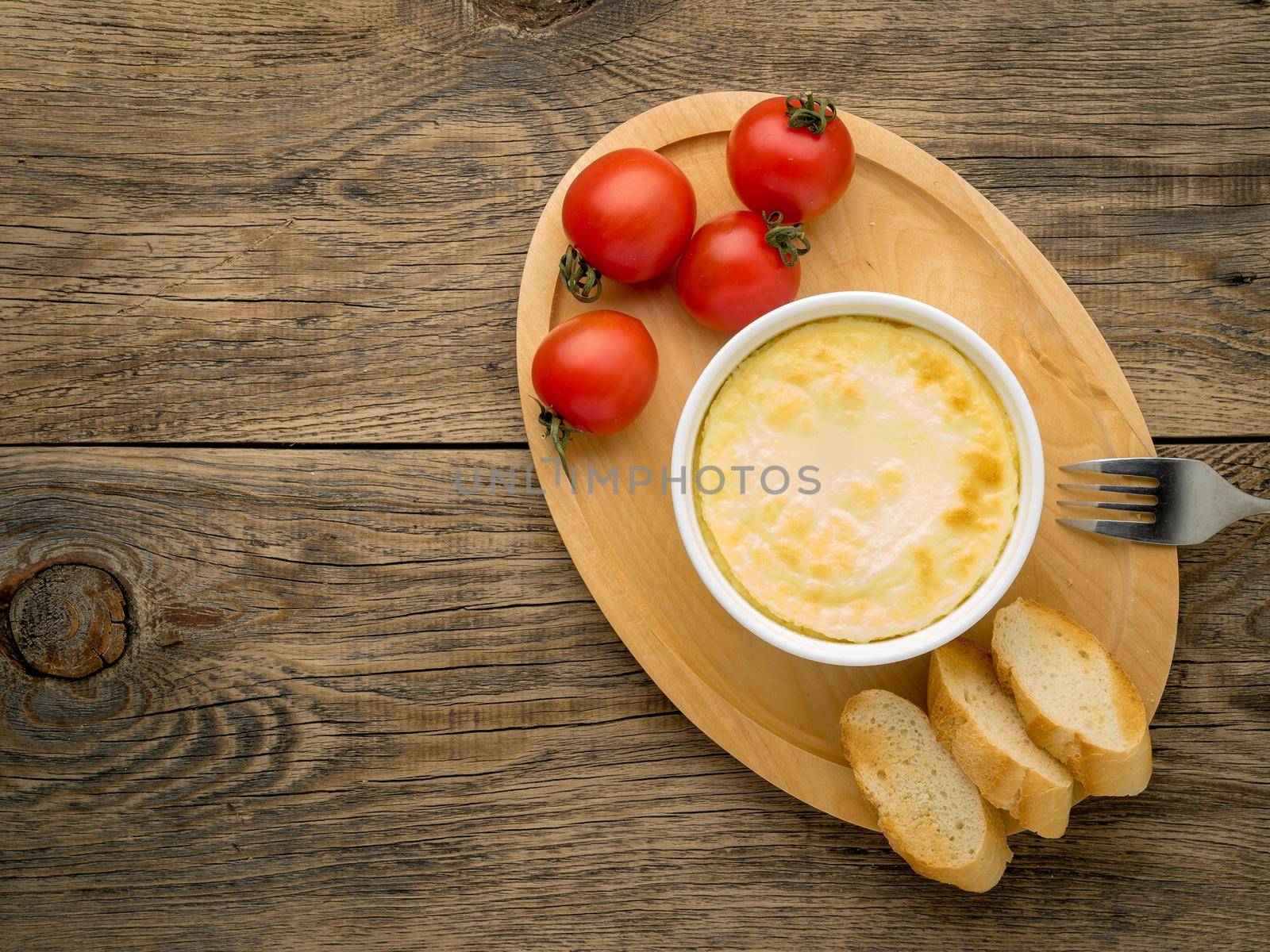 wood plate with oven-baked omelet of eggs and milk, with tomatoes and toast on brown rustic wooden table, top view, copy space by NataBene