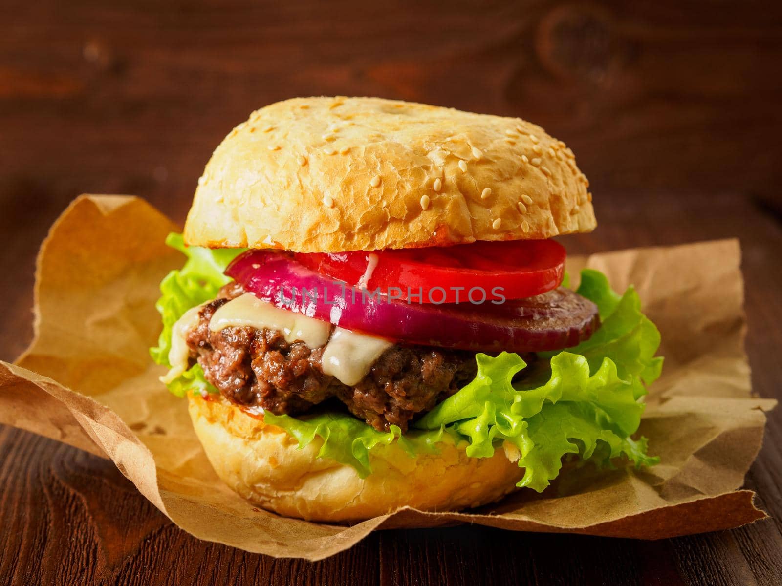 Big delicious homemade burger with beef cutlet, cheese, onion, tomato and lettuce on toasted rolls. American fast food, unhealthy eating. Side view, selective focus by NataBene
