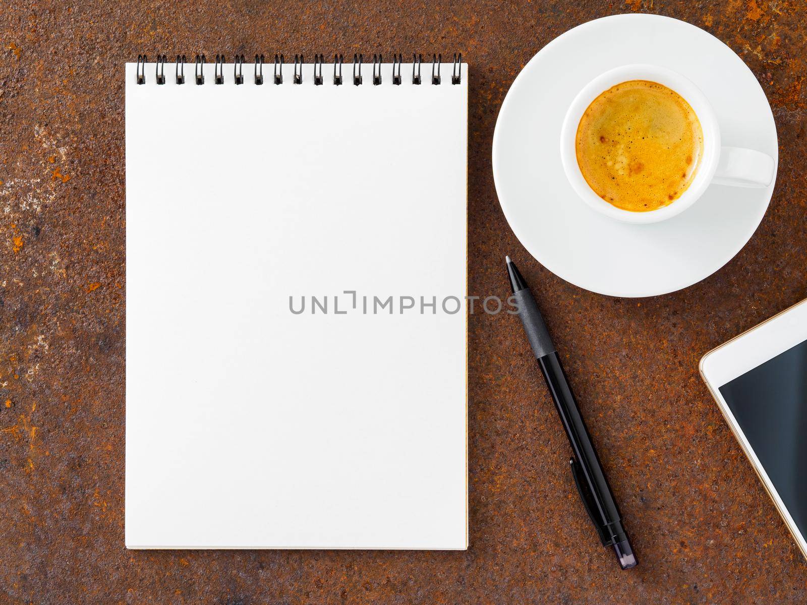 clean white sheet in an open spiral-bound pad, pen, mobile phone and Cup of coffee on the iron of the rusty metal table, top view