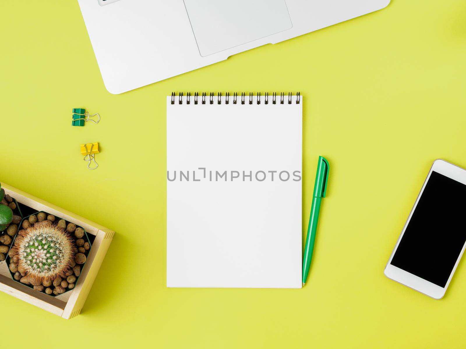 Top view of modern bright yellow office desktop with blank notepad, computer, smartphone. Mock up, empty space by NataBene