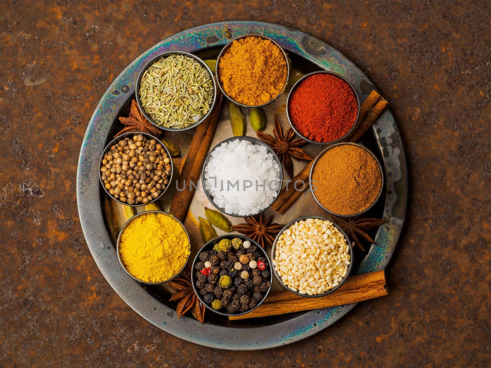 Mix spices on dark brown rusty metal plate - coriander seeds, ground red pepper, salt, black pepper, rosemary, turmeric, curry, coriander. Top view, close up, metall rusty background.
