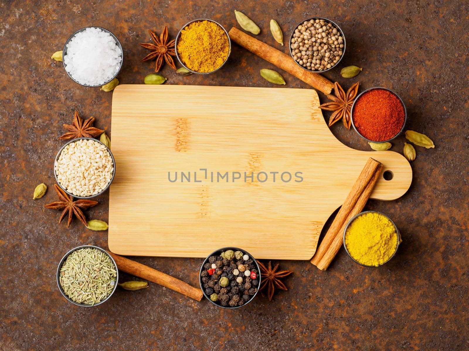 Various Indian spices in metal cups. Empty wooden Board, top view, space for text.