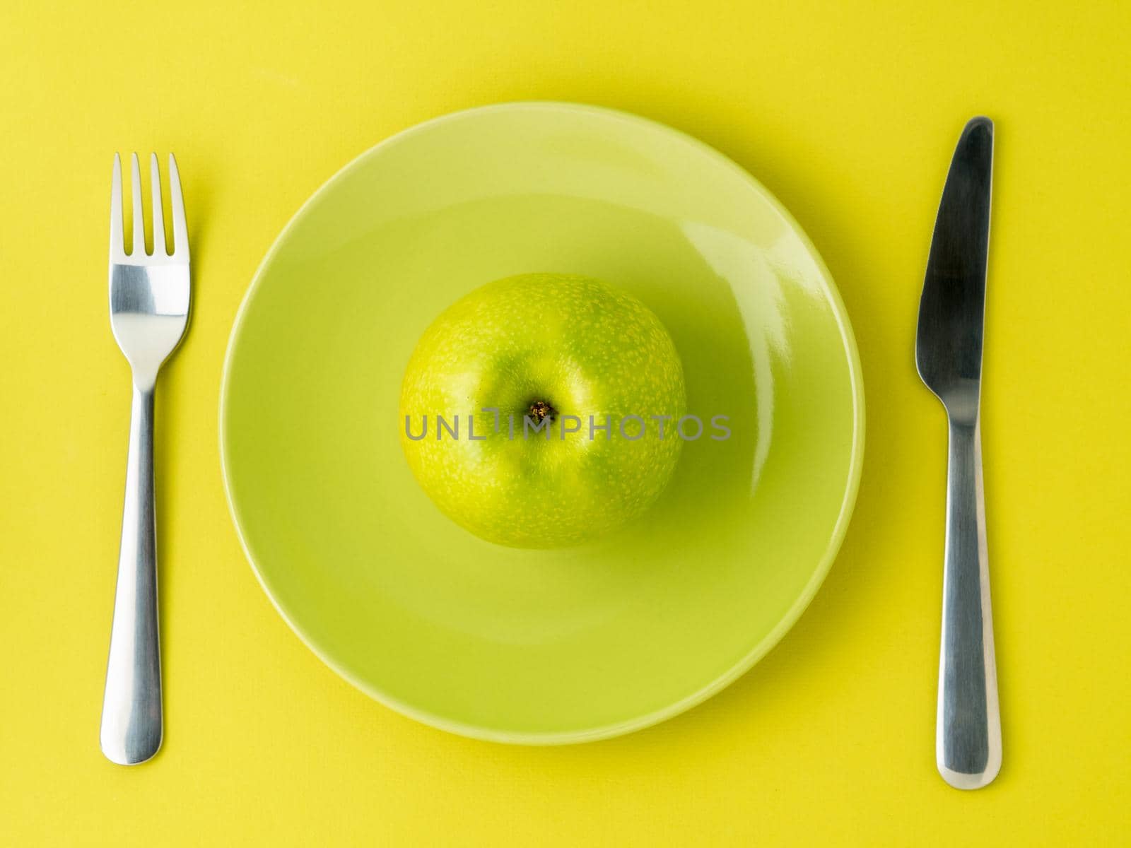 green ripe apples on a bright green plate, knife, fork on colorful yellow and green background, top view