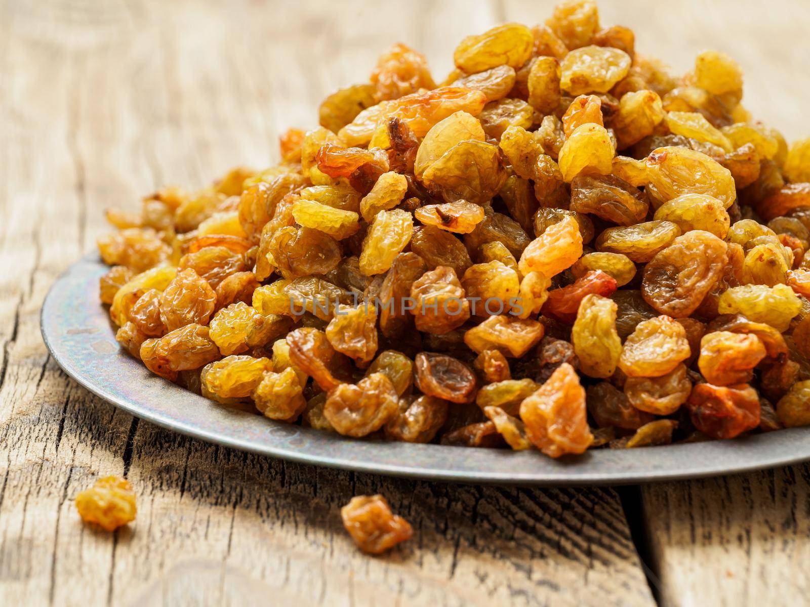 large handful of raisins on a metal tray. A lot of dried fruit on the plate on wooden table, side view, close-up