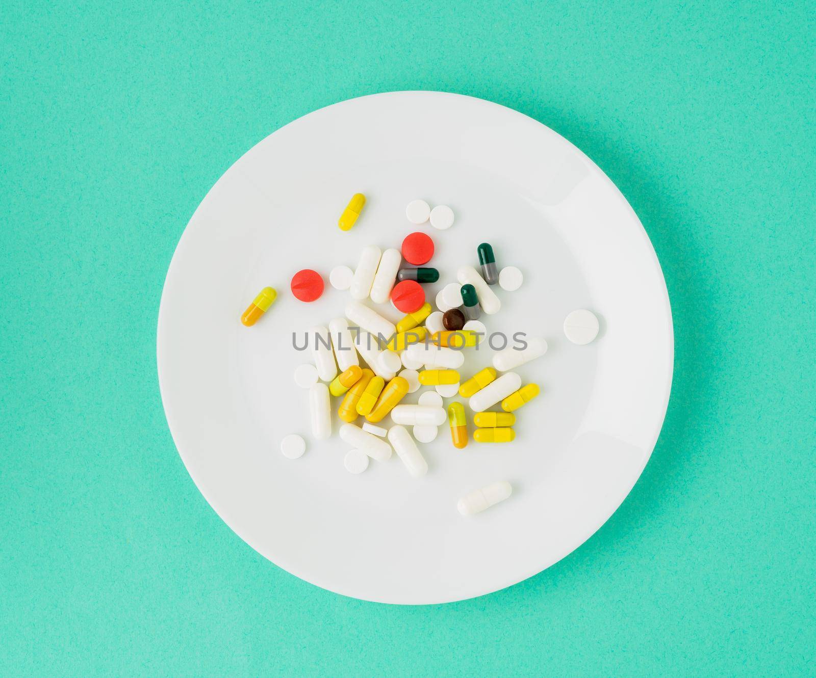 handful of scattered medicines, pills and tablets on white plate on blue background by NataBene