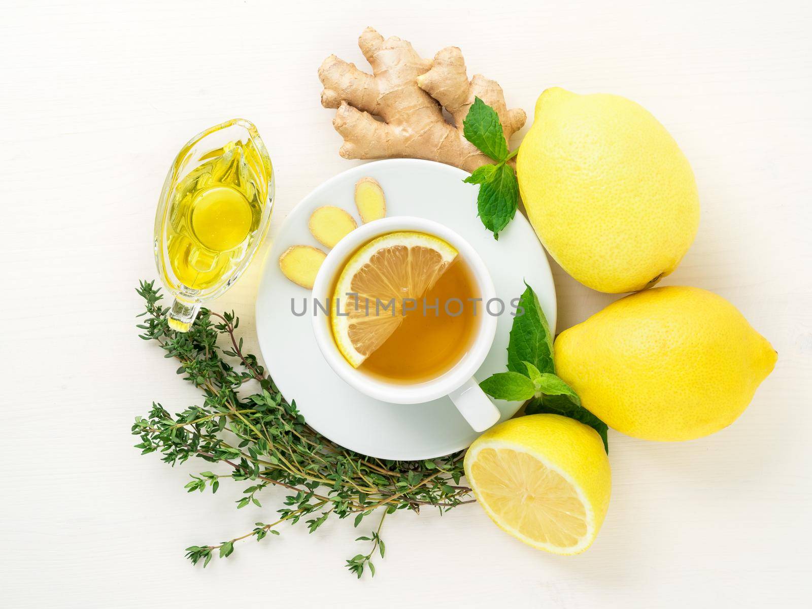 Folk ways to treat colds - cup of tea and a slice of lemon, ginger, mint, honey, herbs, whole lemons and half on a white background, top view. by NataBene