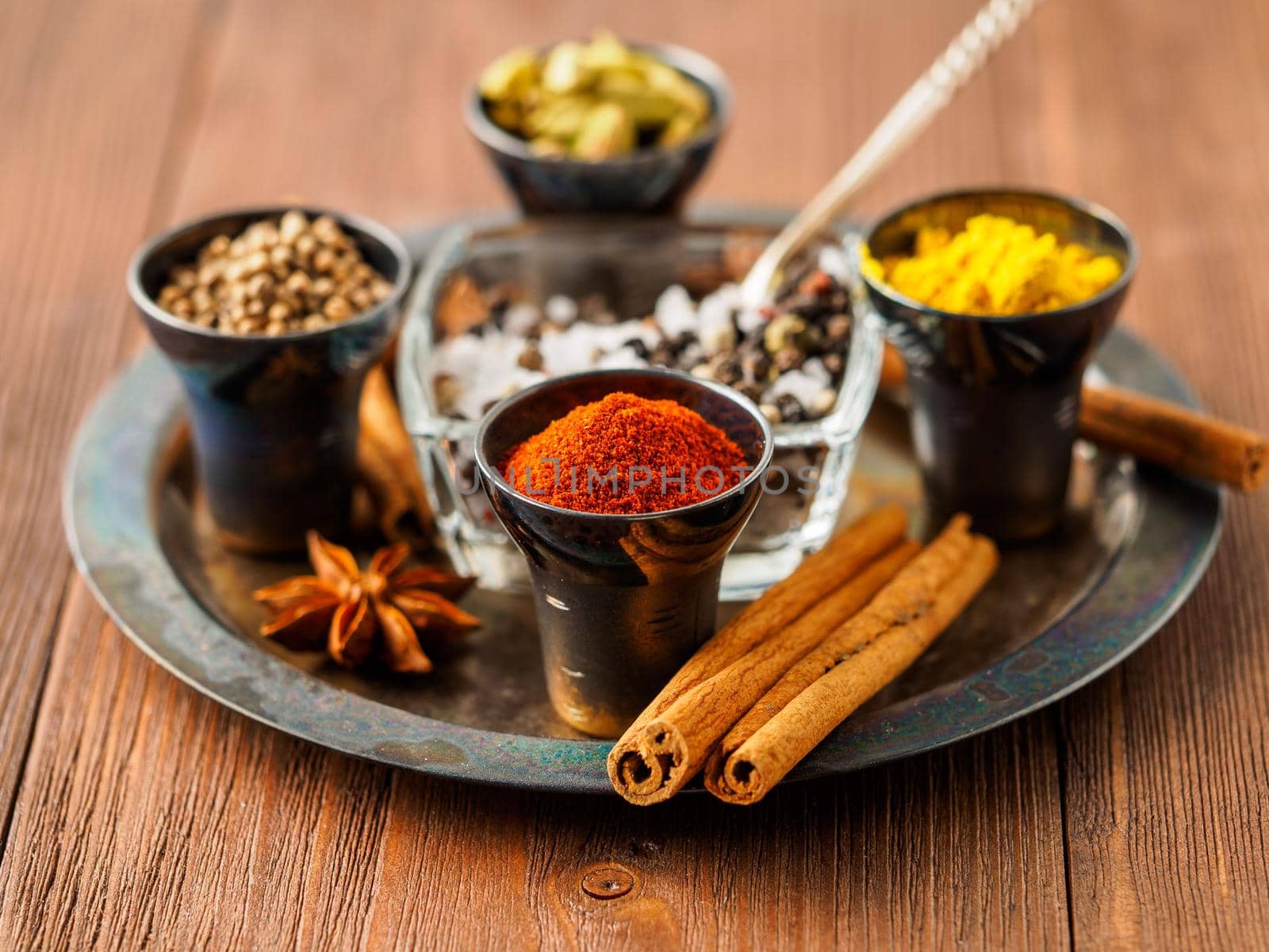 Oriental spice set - coriander, red pepper, turmeric, cinnamon, star anise, rosemary various seasonings in metall cups, on brown wooden table, side view, mcro, selective focus.