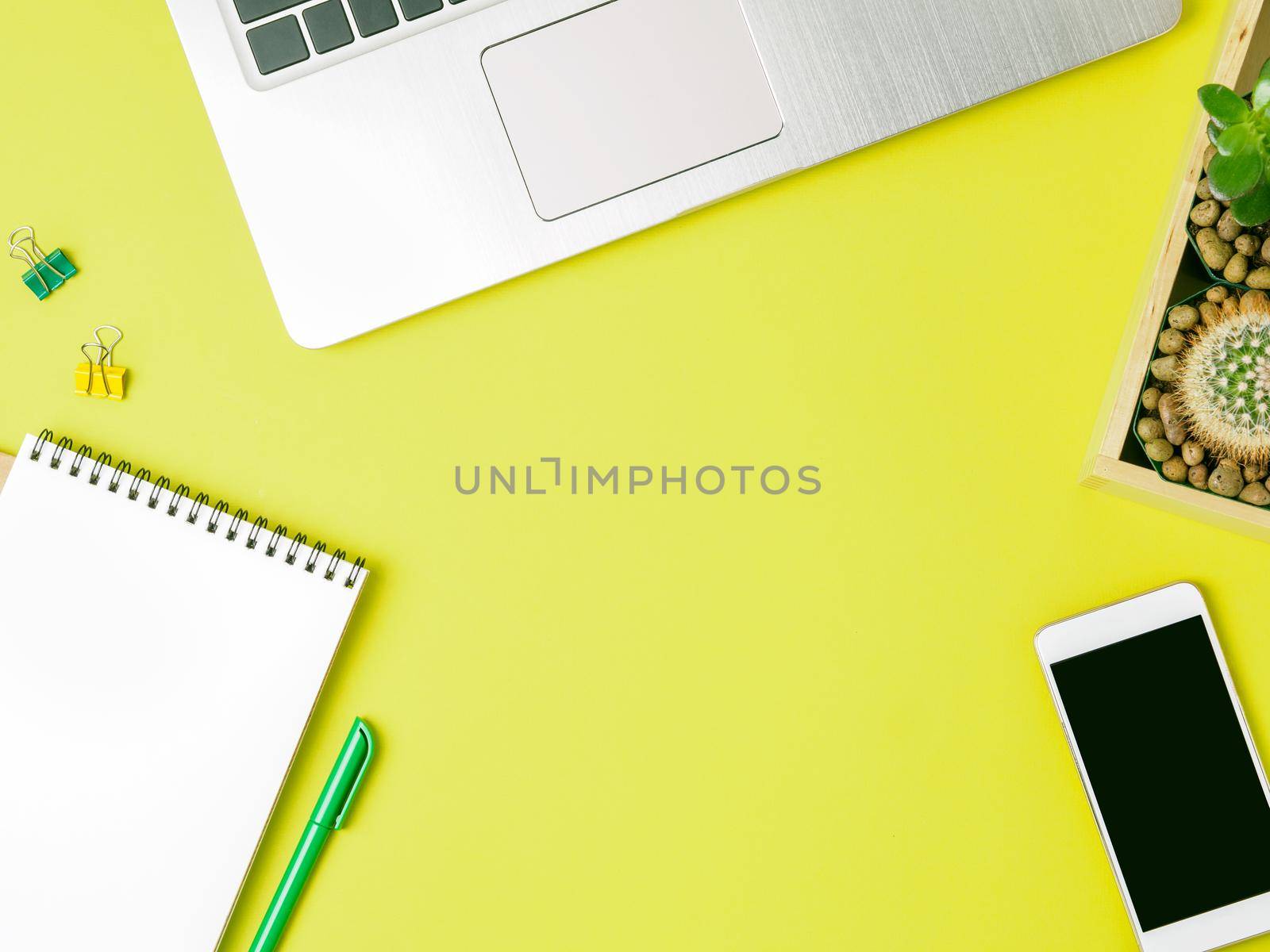 Top view of modern bright yellow office desktop with blank notepad, computer, smartphone. Mock up, empty space by NataBene