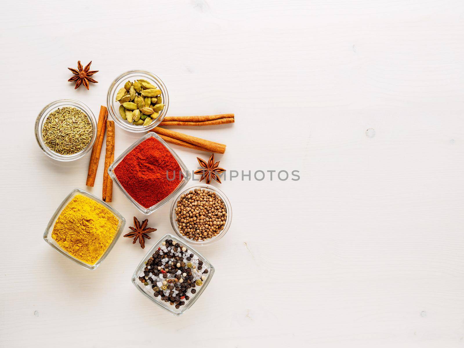 spice set-coriander, red pepper, turmeric, cinnamon, star anise, rosemary various seasonings in glass cups, on white wooden table, top view, blank space for text. by NataBene