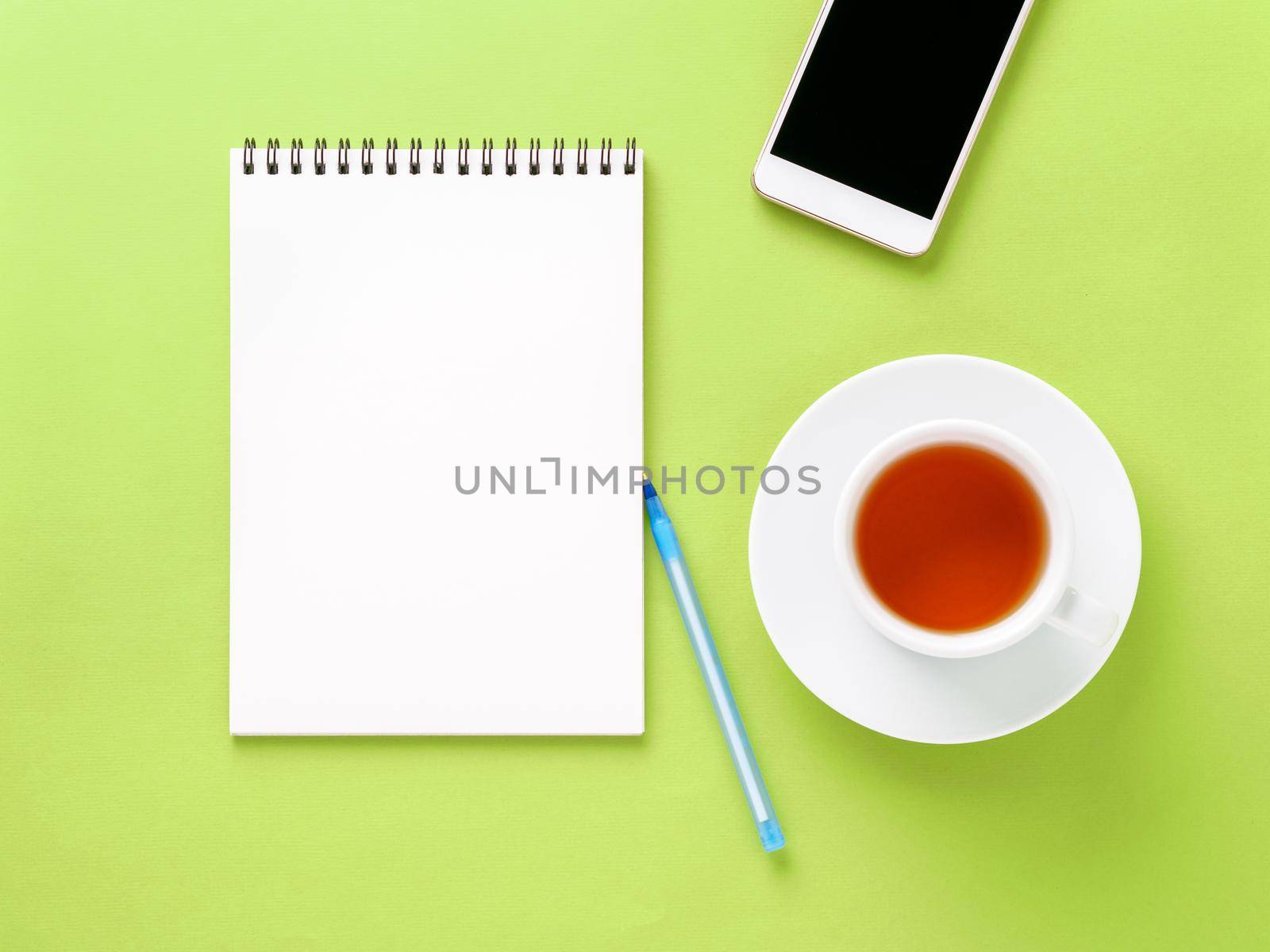 Top view of modern bright green office desktop with blank notepad, cup of tea, smartphone. Mock up, empty space