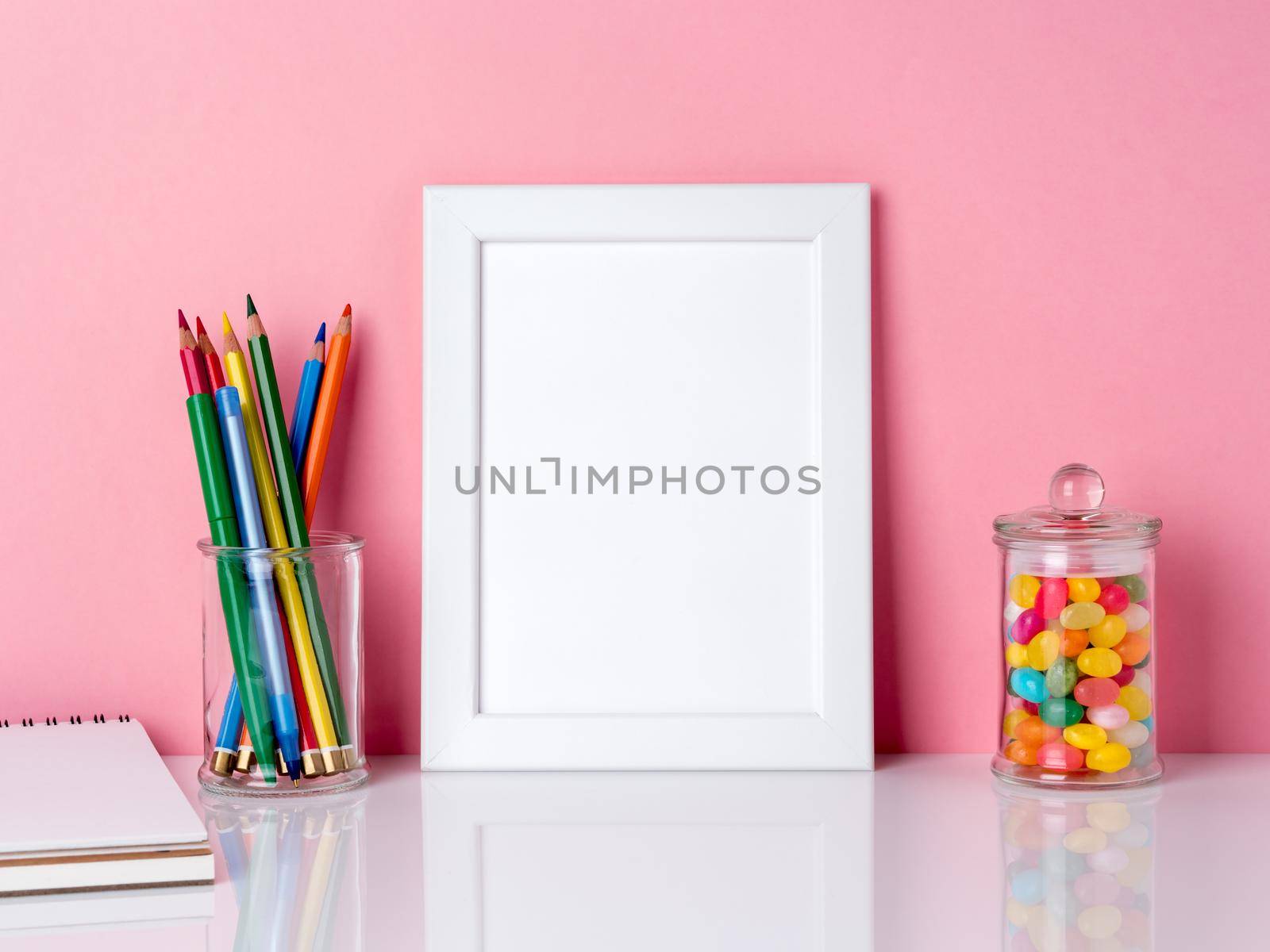 Blank white frame and crayon in jar, candys on a white table against the pink wall with copy space by NataBene