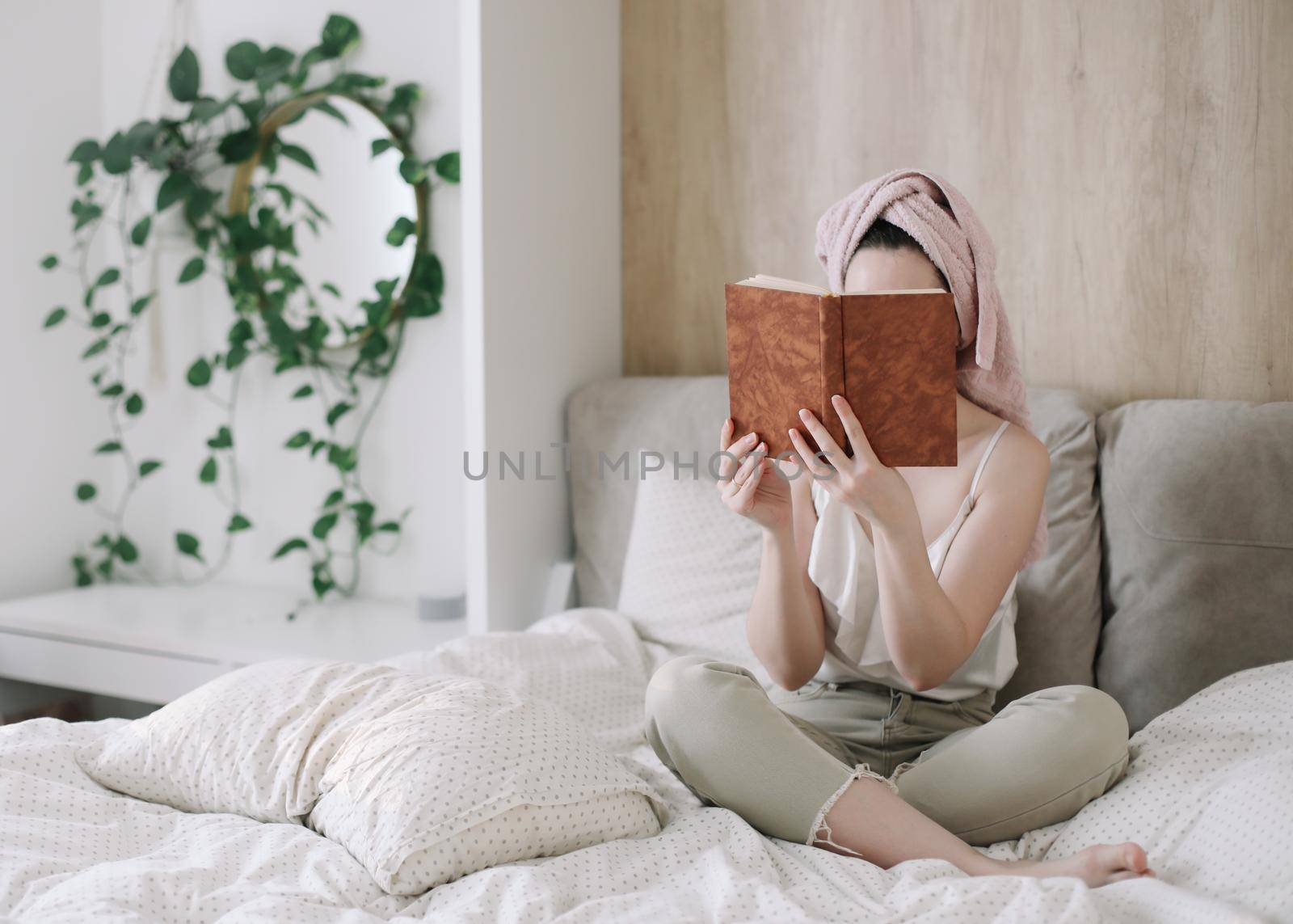 Morning book reading. Young woman with a towel on head reading book in bed in the morning. Lazy weekend at home with book. Close up, copy space, interior background.