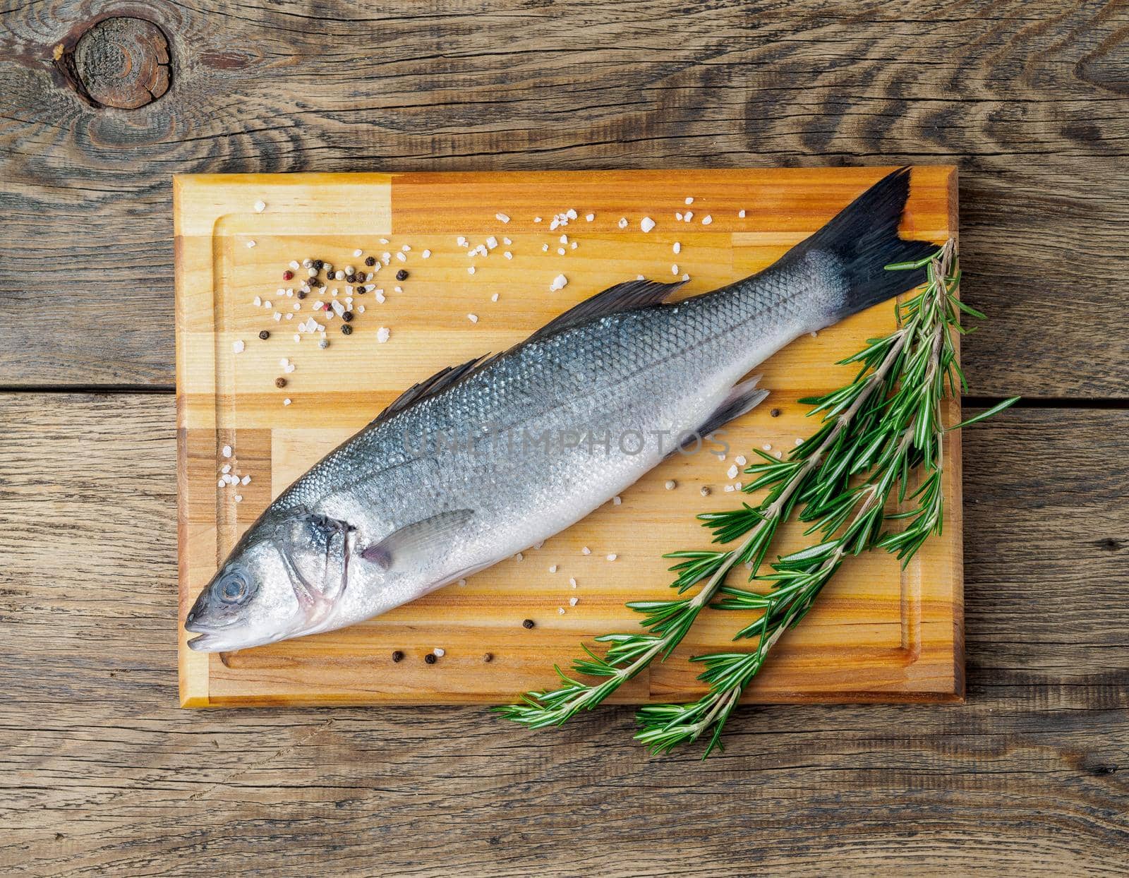 fresh, raw, saltwater fish, sea bass on a wooden cutting board on old wooden aged, rustic table, top view by NataBene