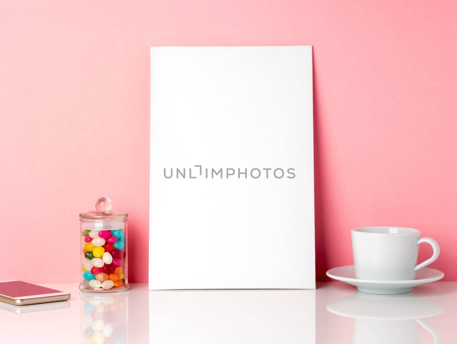 Blank white frame and candys in jar, cup of coffee or tea on a white table against the pink wall with copy space by NataBene