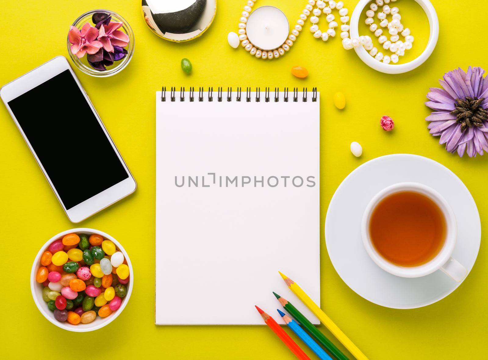 Cozy corner for a girl with a notebook, smartphone, flowers, jewelry and sweets. Desktop for creativity, ideas, creativity, dreams. Bright yellow background, top view, flat lay, empty place for text.