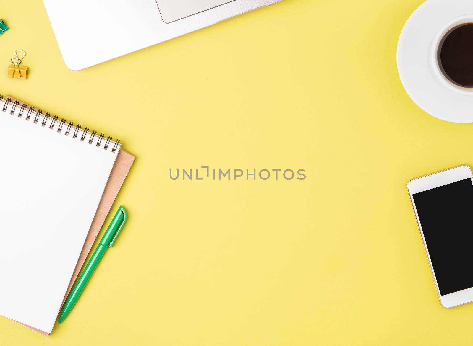Top view of modern bright yellow office desktop with blank notepad, computer, smartphone. Mock up, empty space by NataBene