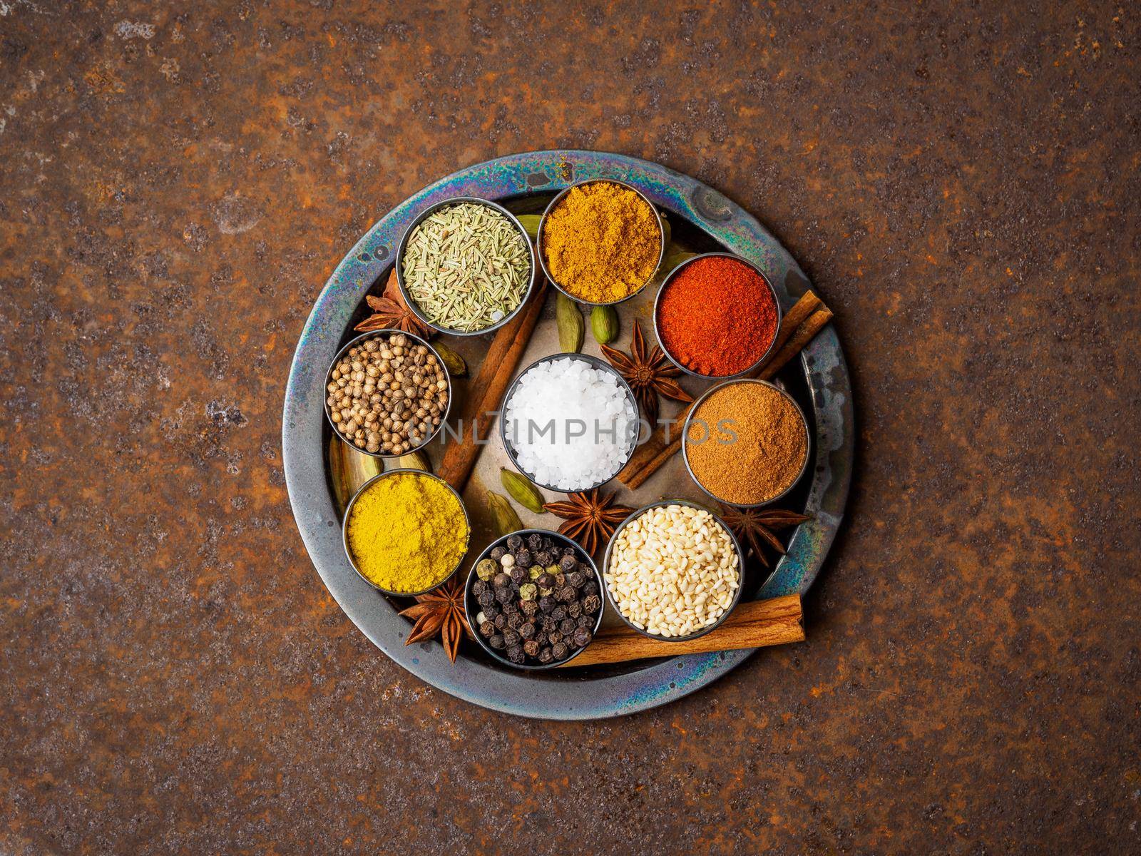 Mix spices on round metal plate - coriander seeds, ground red pepper, salt, black pepper, rosemary, turmeric, curry. Top view, close up, metall rusty background. by NataBene