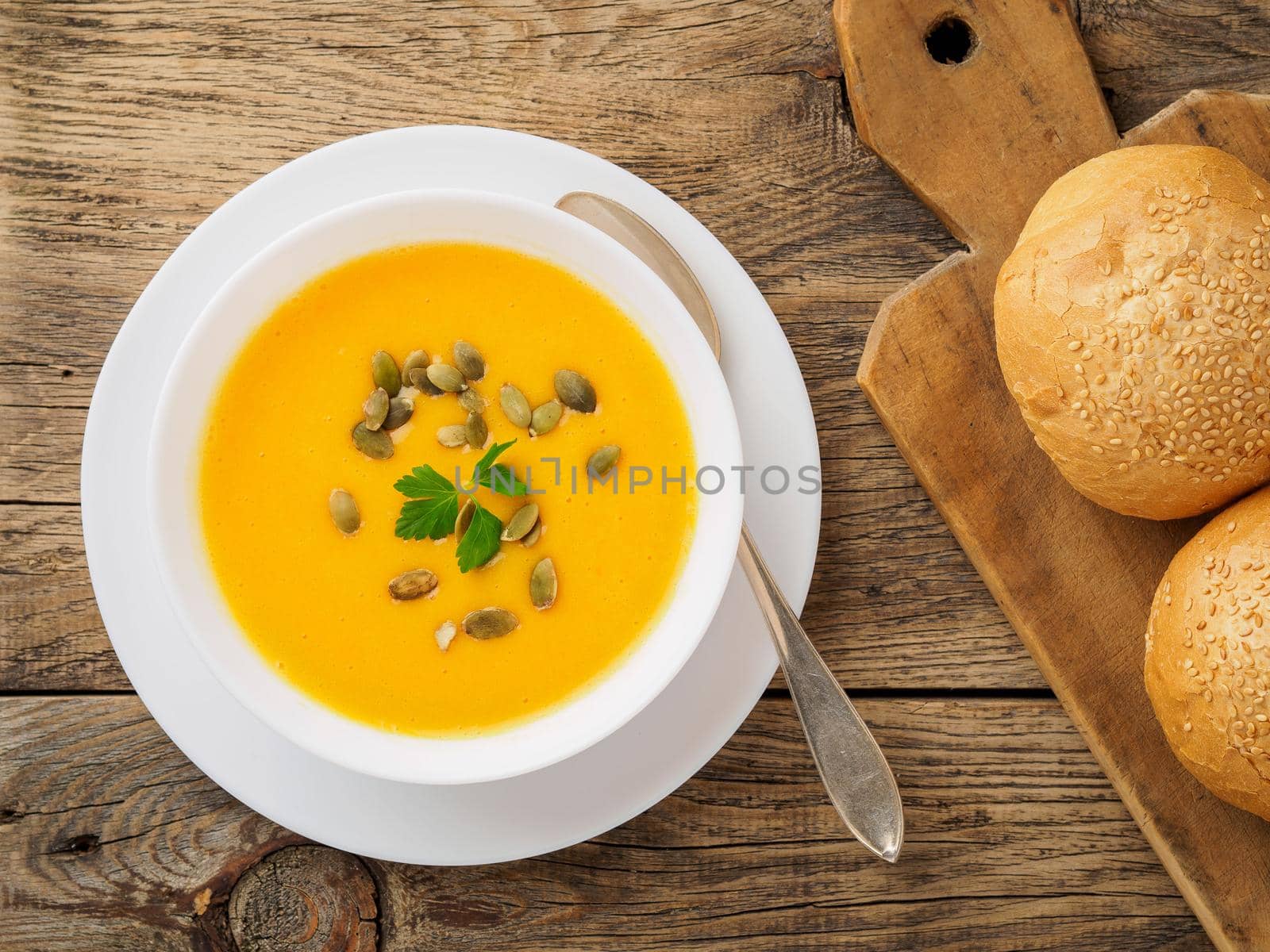 white bowl of pumpkin soup, garnished with parsley and sunflower seeds on wooden background by NataBene