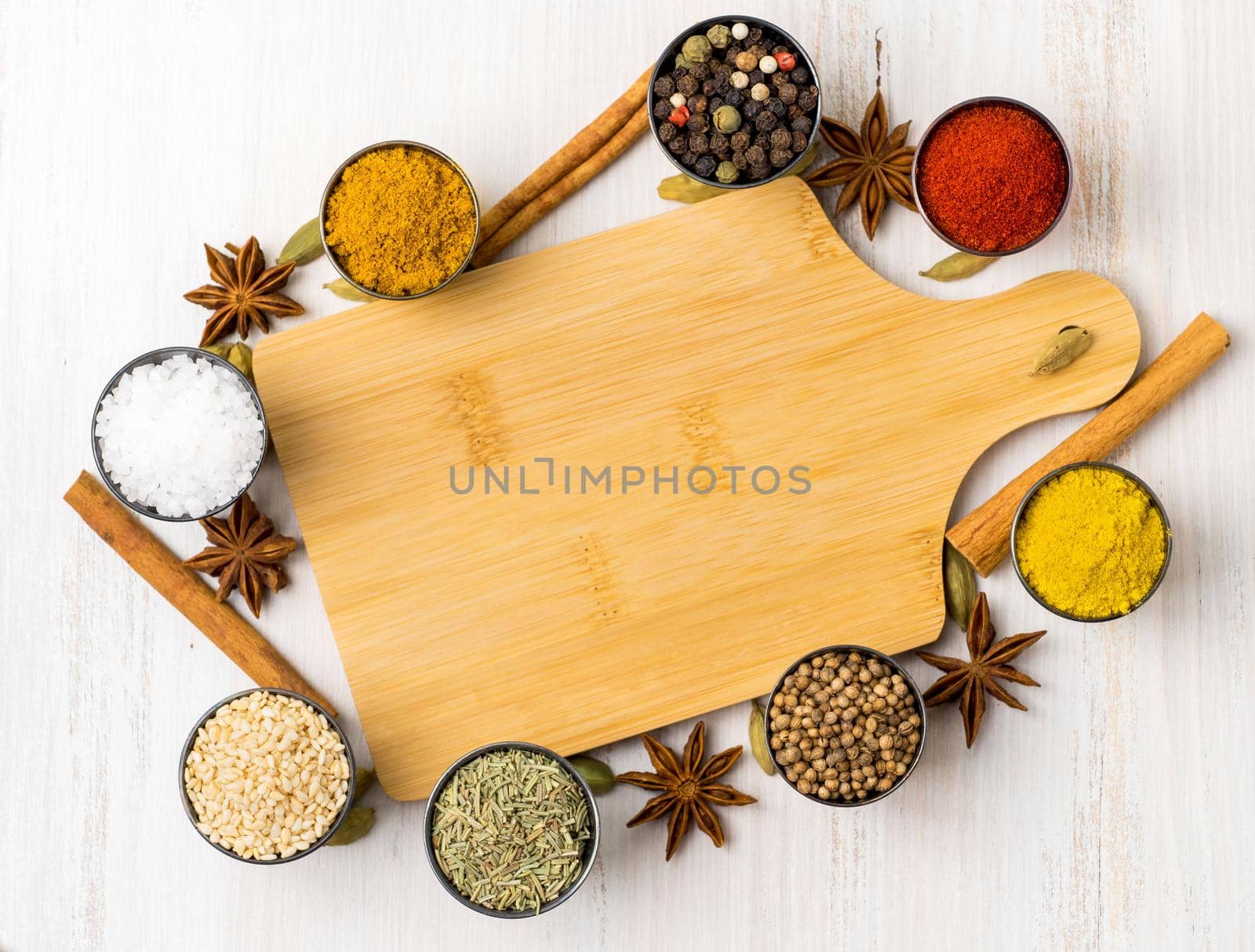 Various Indian spices in metal cups. Empty wooden Board, seasoning on white wooden table. top view, space for text.