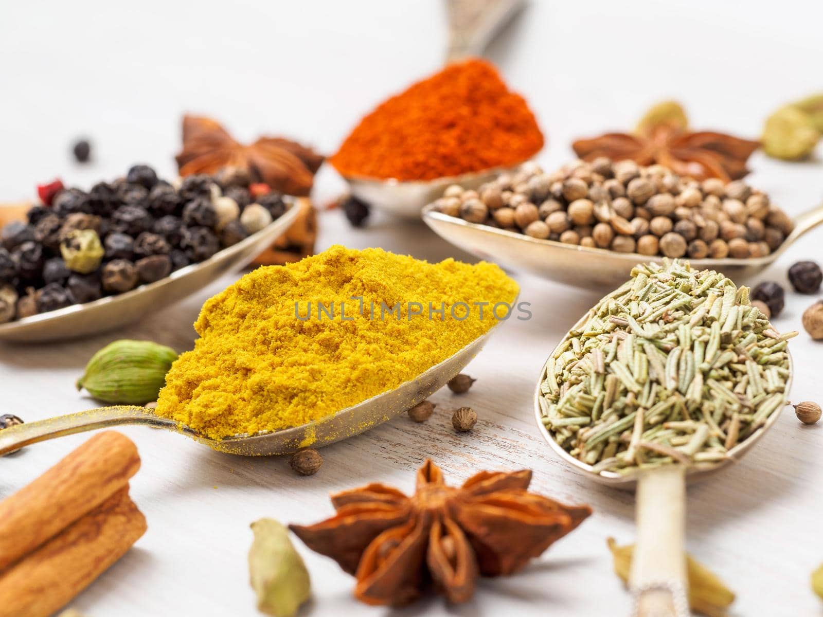 Mix of Indian spices in spoons on white wooden table, side view, selective focus, macro. Seasonings turmeric, close up