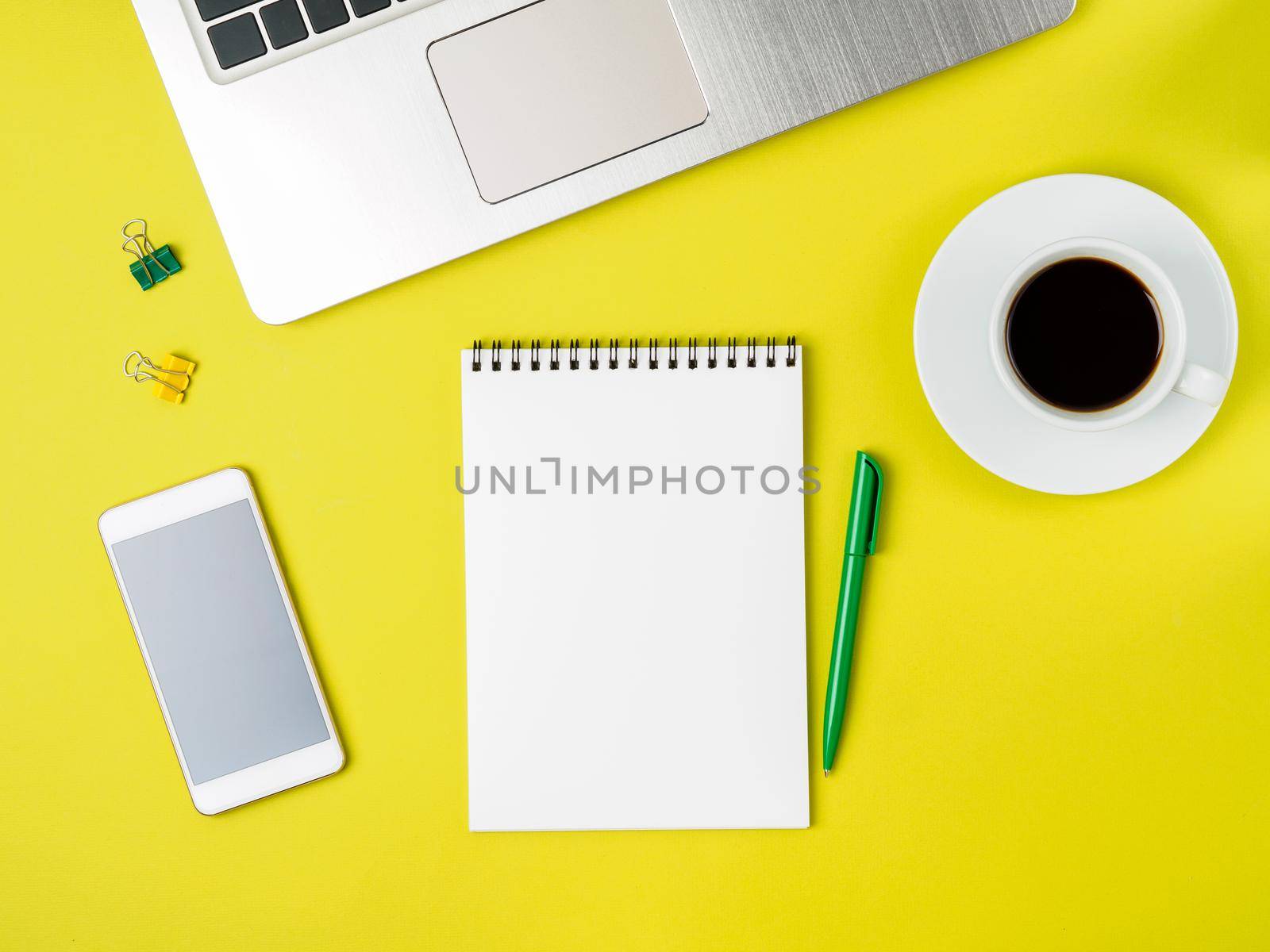 Top view of modern bright yellow office desktop with blank notepad, computer, smartphone. Mock up, empty space by NataBene