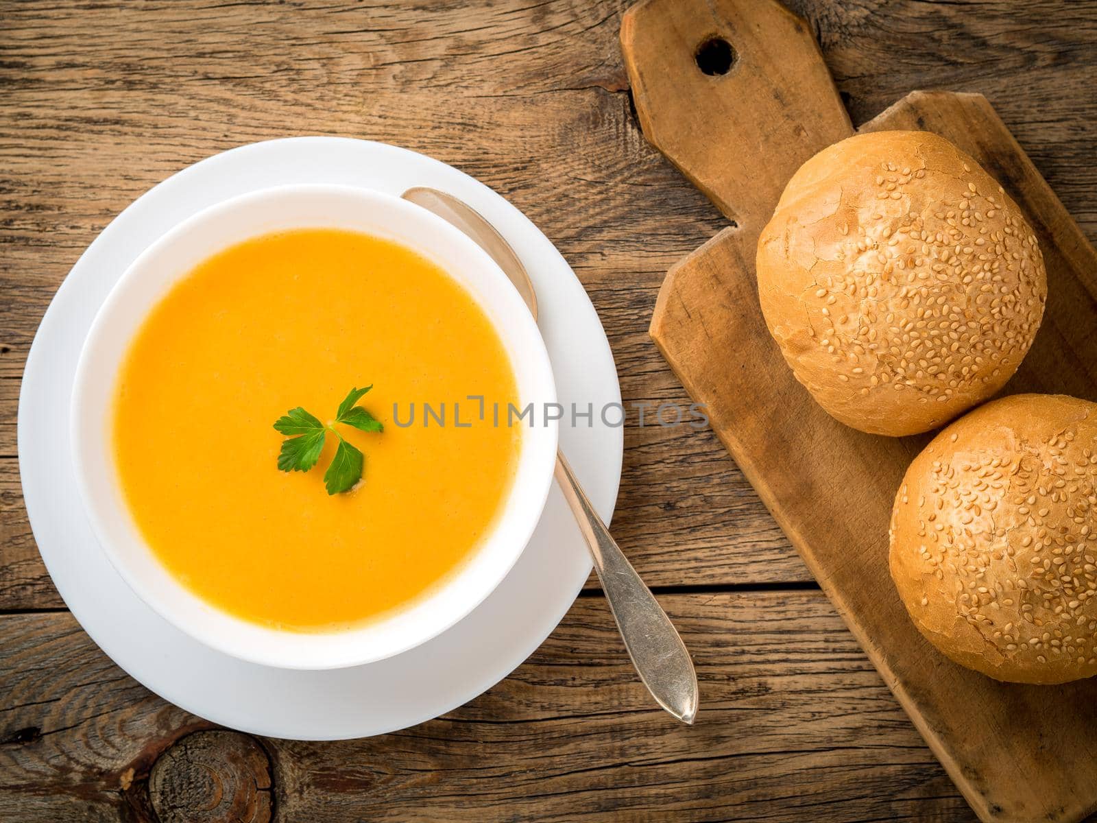 white bowl of pumpkin soup, garnished with parsley on wooden background, top view.