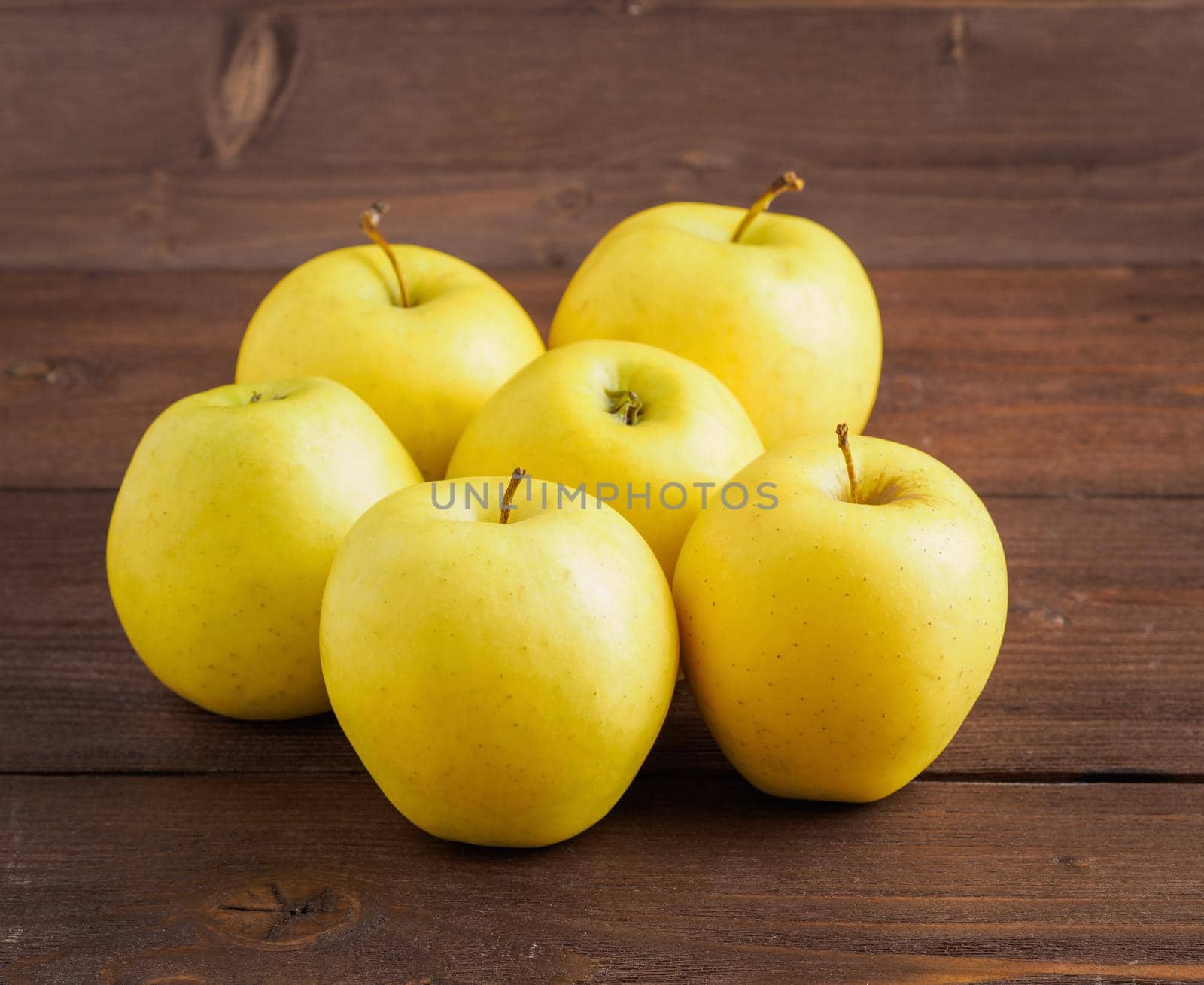 Golden Delicious. Juicy ripe fresh yellow apples on a brown wooden background, side view. by NataBene