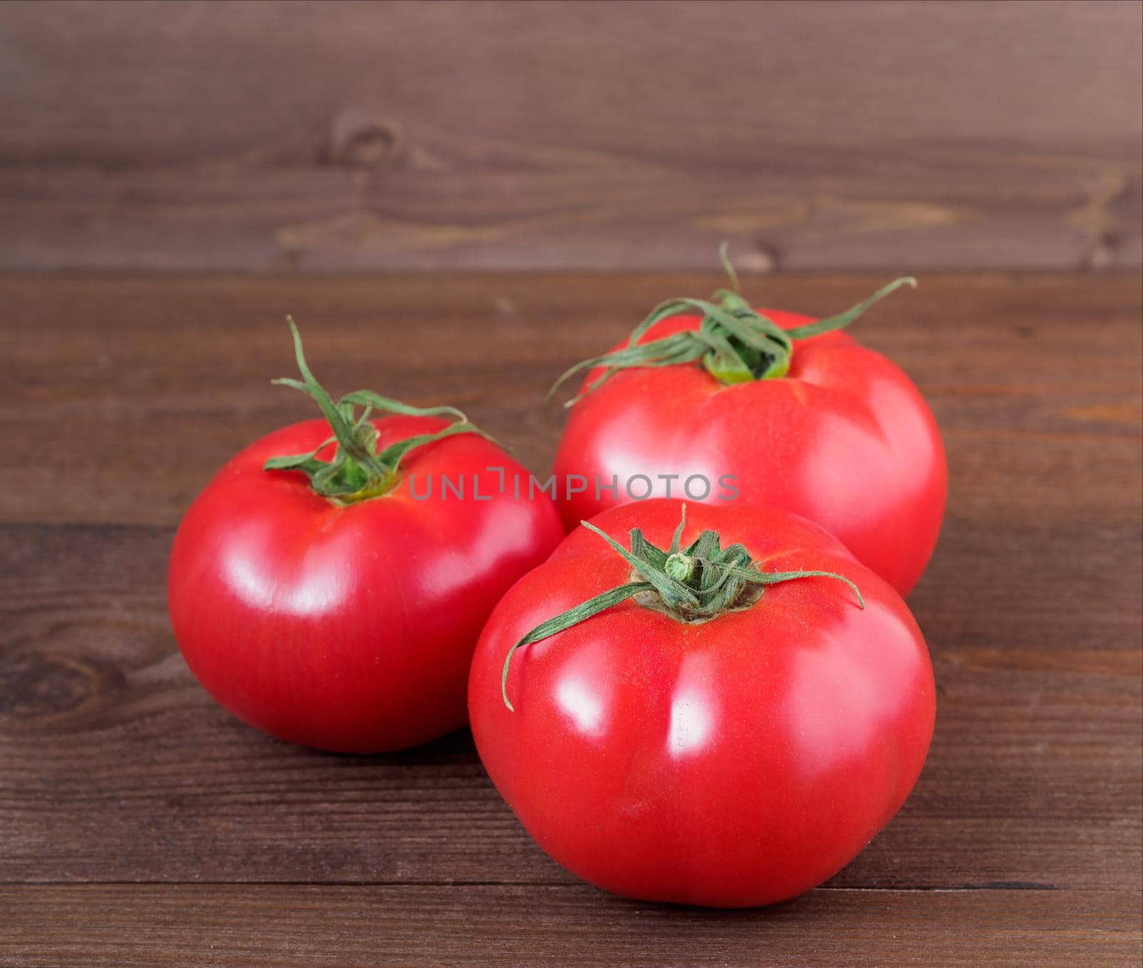 three ripe fresh red tomatoes on wooden brown background