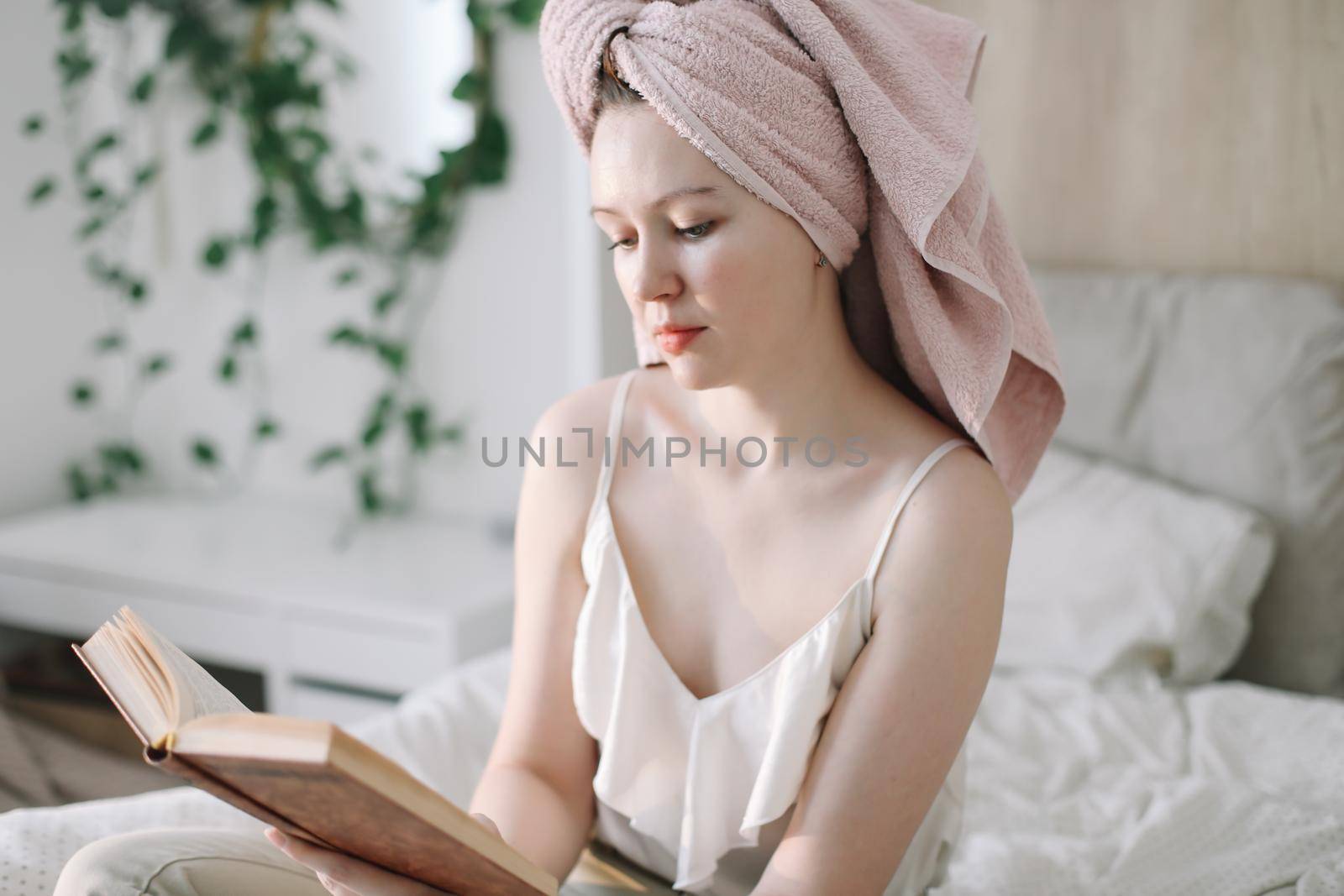 Morning book reading. Young woman with a towel on head reading book in bed in the morning. Lazy weekend at home with book. Close up, copy space, interior background.