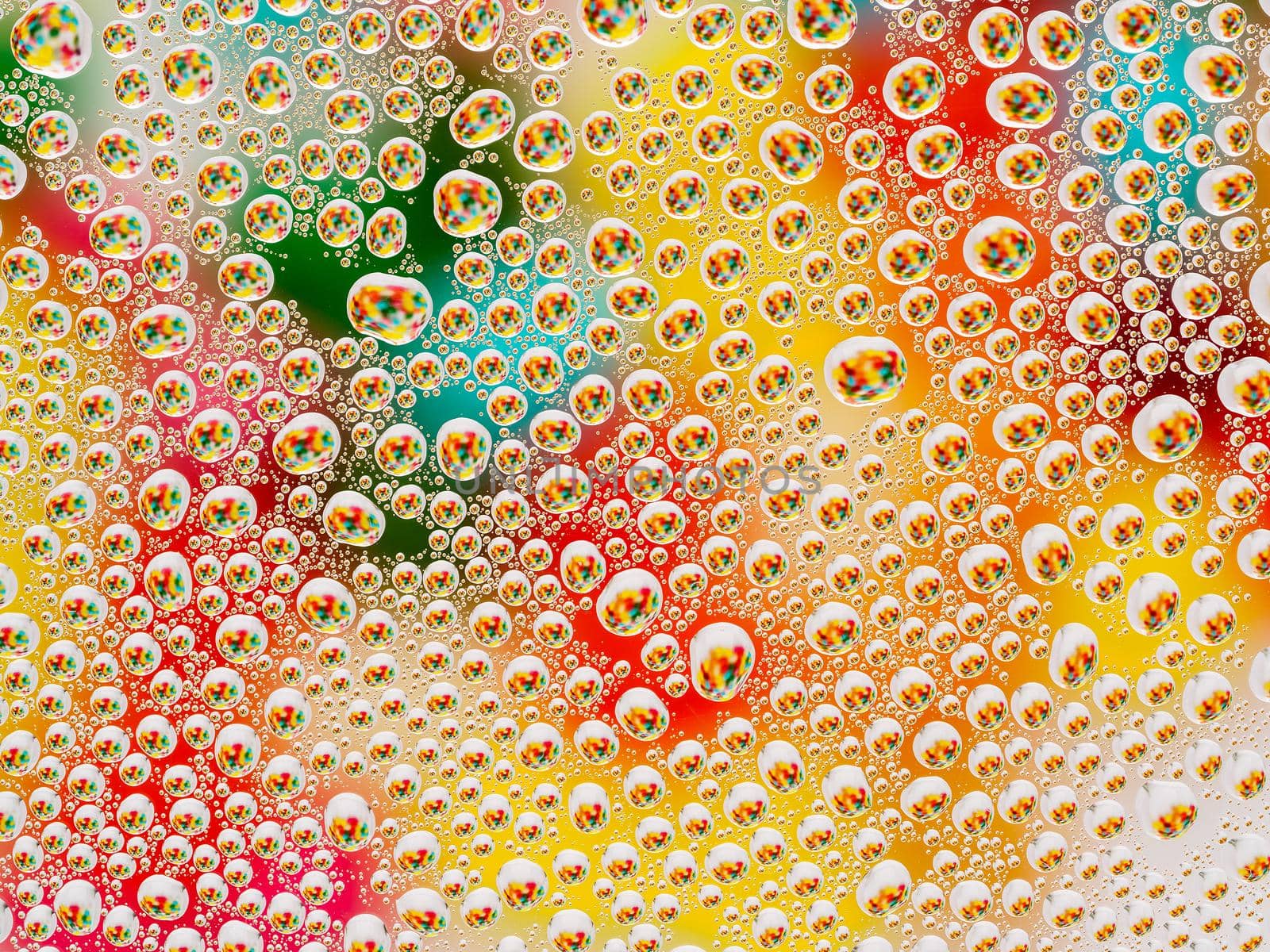 Abstract colorful vivid background with large and small spherical convex drops of water on the glass. Macro, top view, close up.