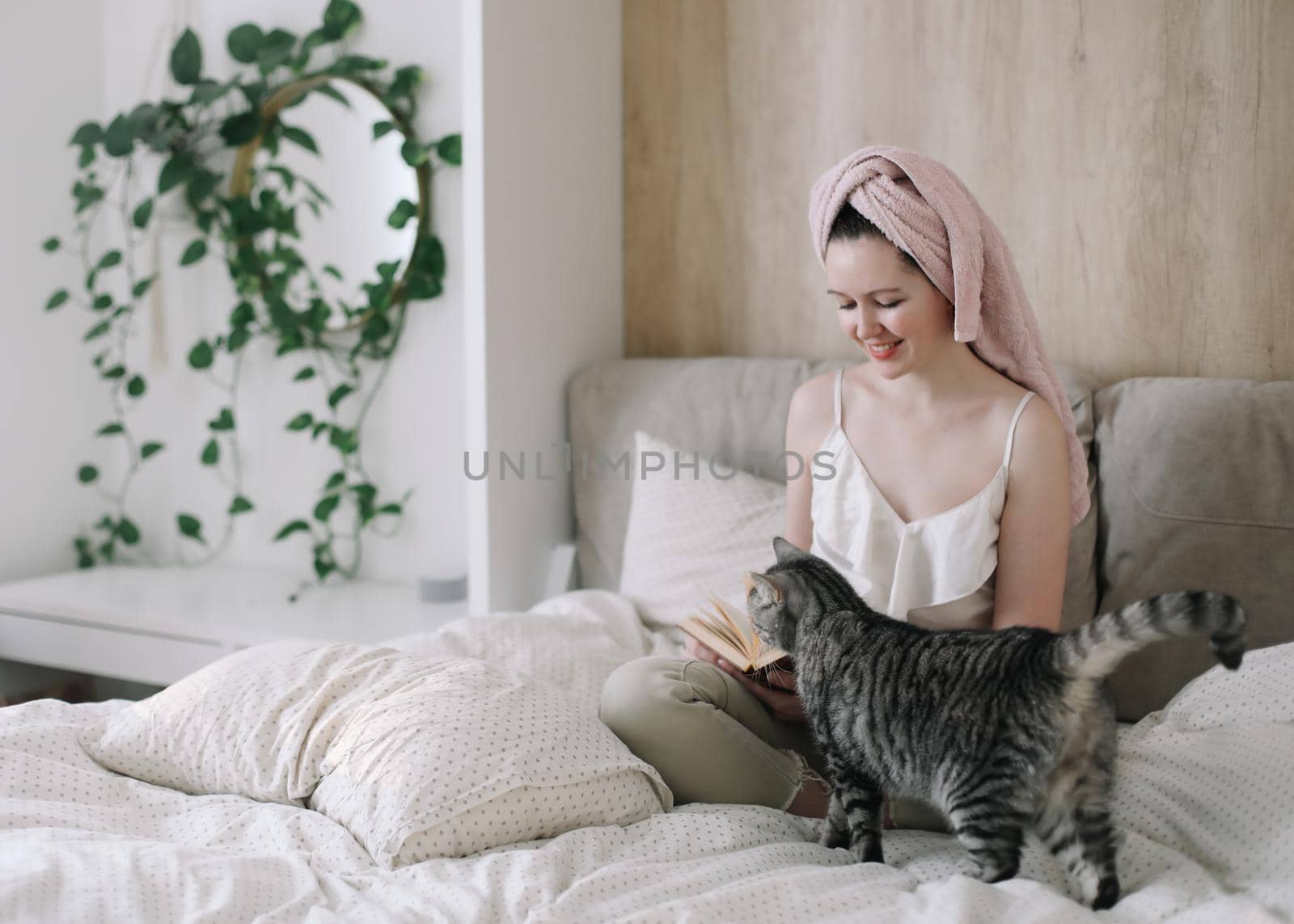 Young woman and her adorable cat reading book and resting in bed. Lazy weekend at home with loved pet concept. Close up, copy space, interior background. Love, togetherness and pets indoors by paralisart