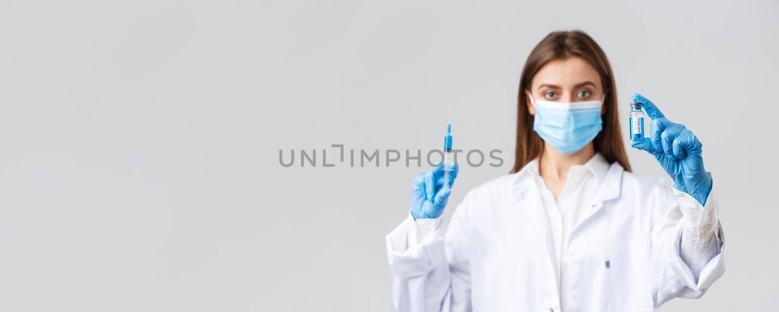 Covid-19, preventing virus, healthcare workers and quarantine concept. Doctor in medical mask, rubber gloves and scrubs showing ampoule with coronavirus vaccine, hold syringe, making patient a shot.