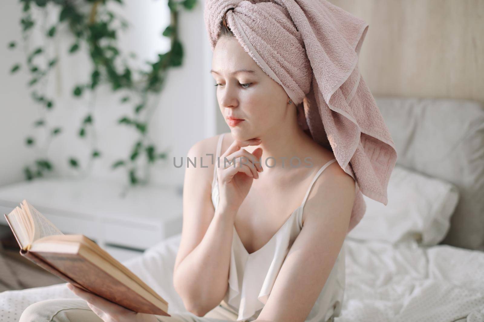 Morning book reading. Young woman with a towel on head reading book in bed in the morning. Lazy weekend at home with book. Close up, copy space, interior background.
