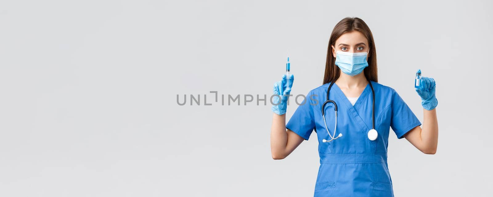 Covid-19, preventing virus, healthcare workers and quarantine concept. Confident, professional female doctor, nurse in clinic wearing scrubs and medical mask, showing coronavirus vaccine and syringe.