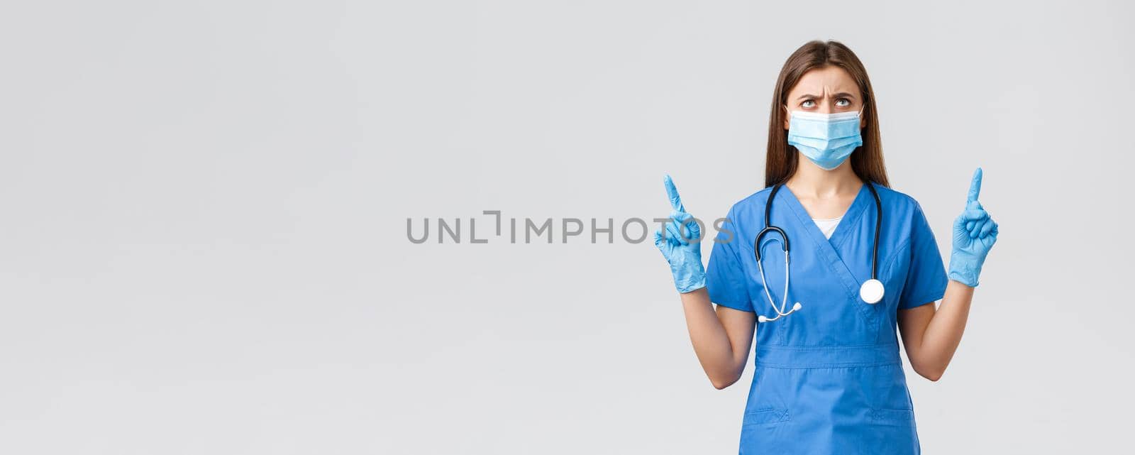 Covid-19, preventing virus, health, healthcare workers and quarantine concept. Concerned and disappointed female nurse or doctor in blue scrubs, medical mask, frowning looking up displeased by Benzoix