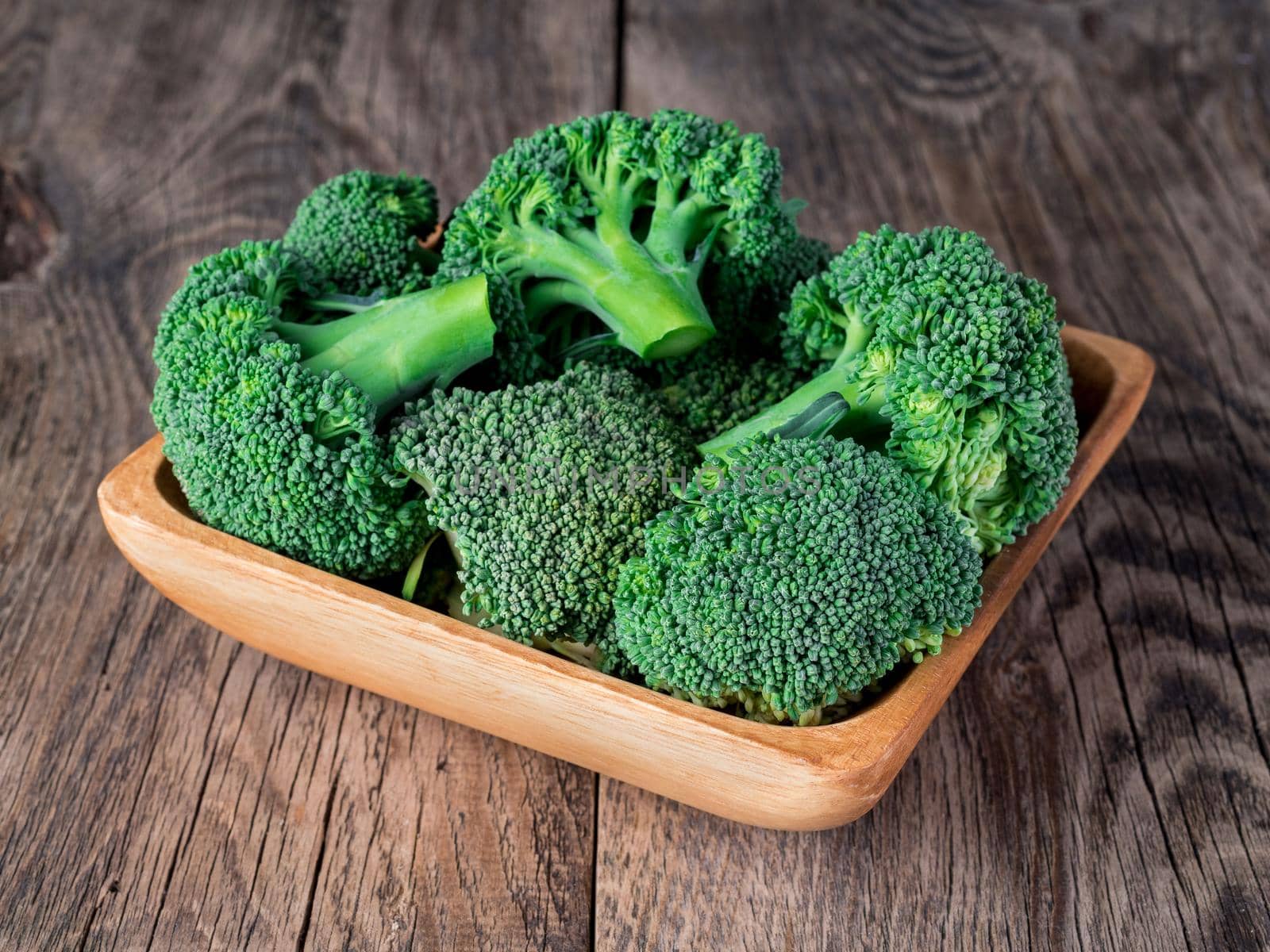 fresh raw green broccoli in wooden bowl on wooden background by NataBene