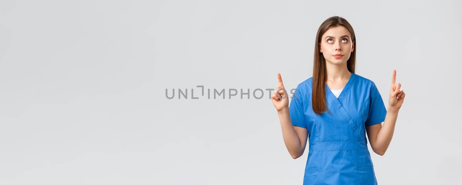 Healthcare workers, prevent virus, covid-19 test screening, medicine concept. Concerned, serious and focused female doctor or nurse in blue scrubs, pointing fingers and looking up at banner.