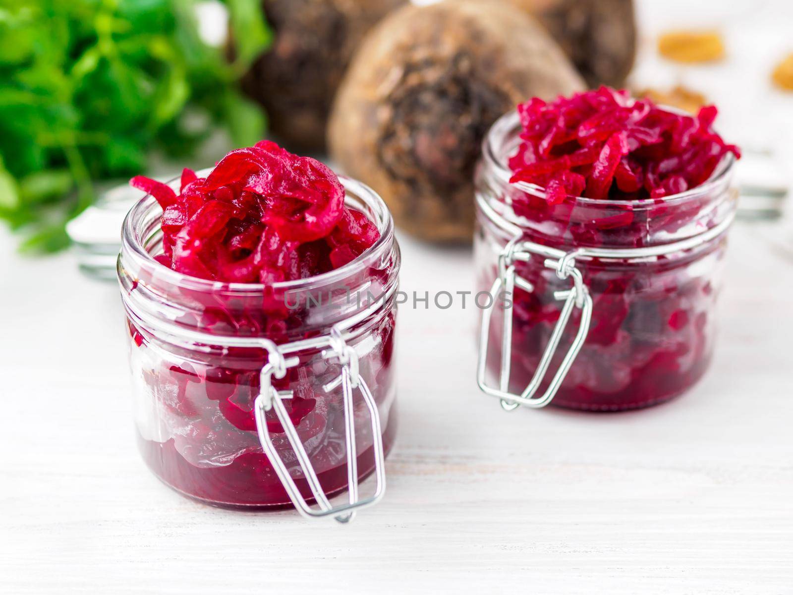 Fresh salad of grated boiled beetroot in glass jars, white wooden background, side view.