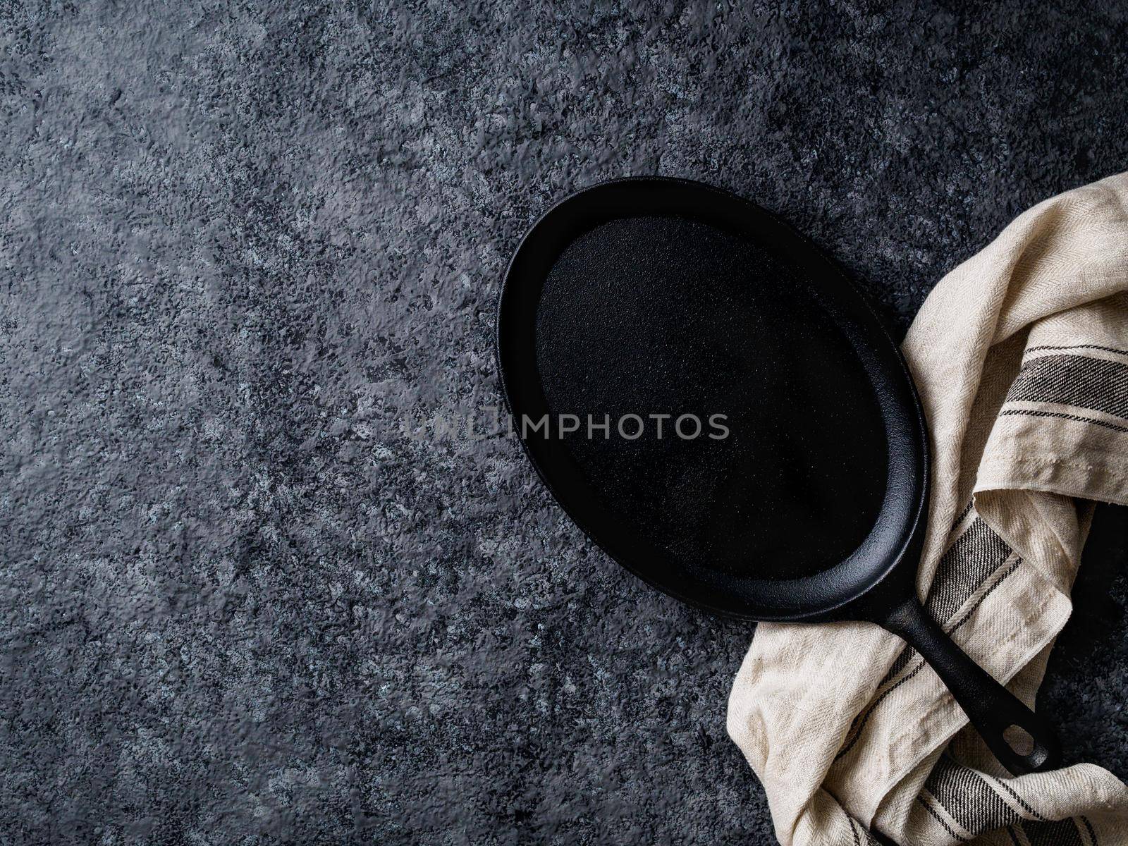 empty oval cast iron frying pan on dark grey concrete background, top view, blank space for text by NataBene